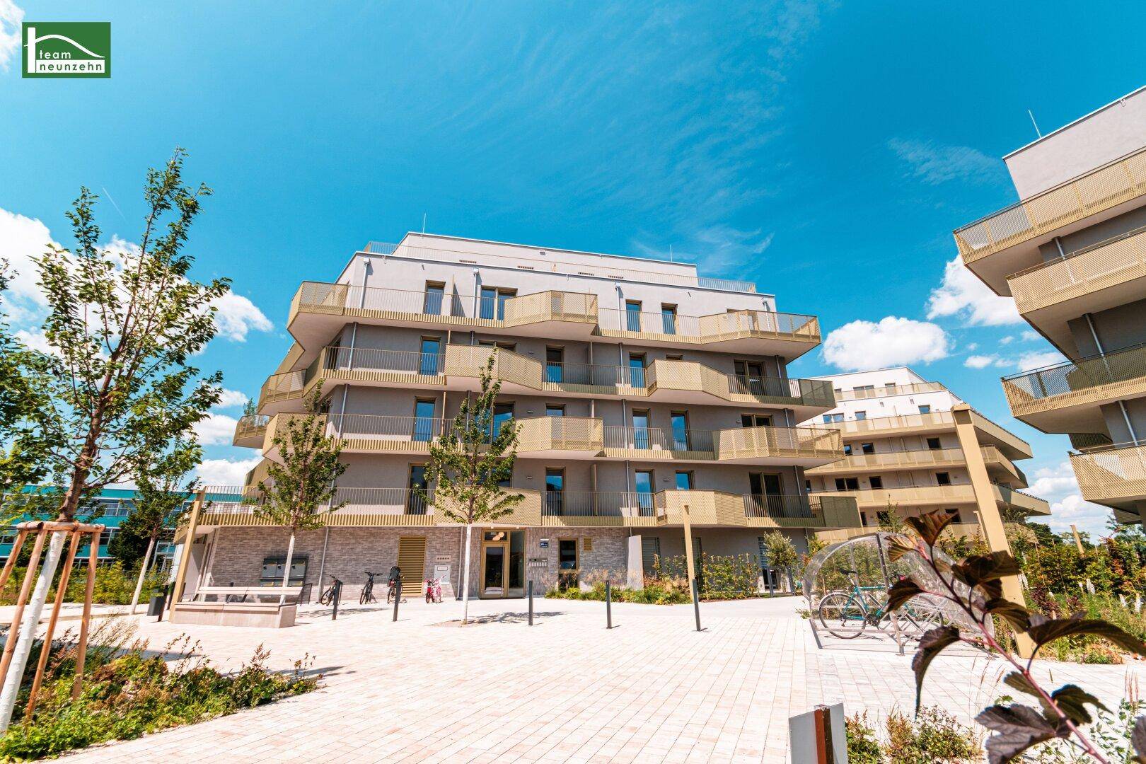 Modernes Mehrfamilienhaus mit mehreren Etagen und Balkonen unter blauem Himmel.