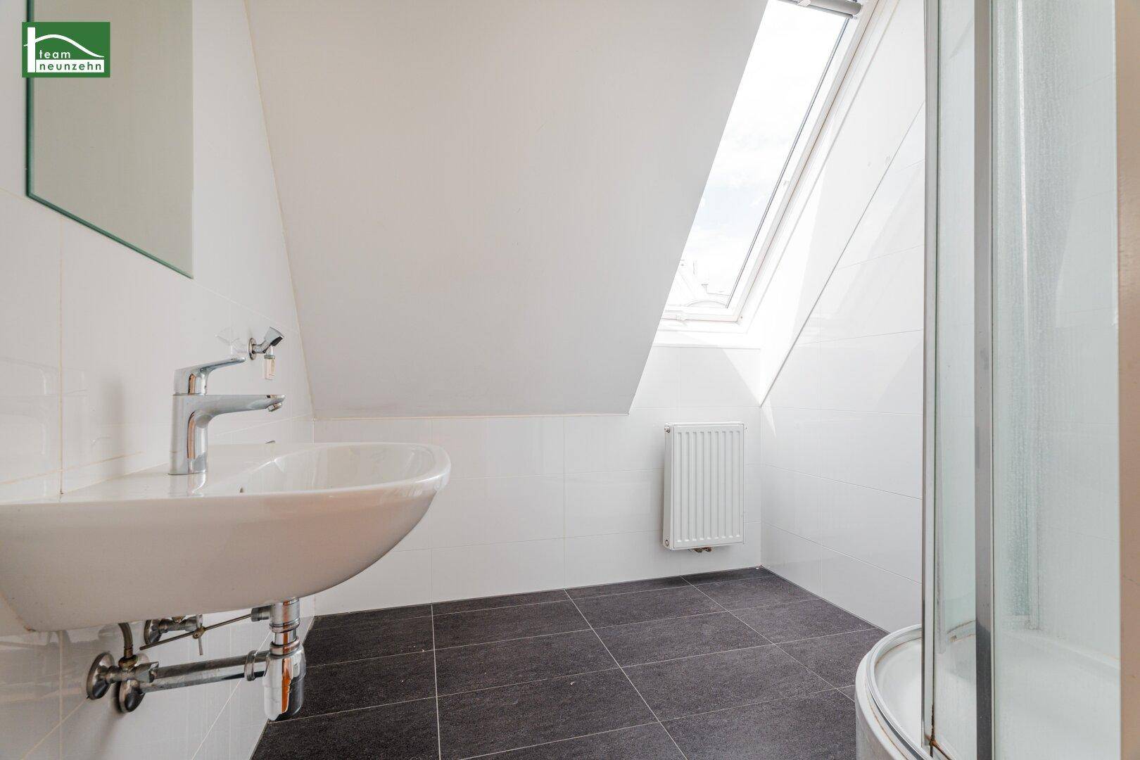 Modernes Badezimmer mit Waschbecken, dunklen Fliesen und Dachfenster, das viel Licht spendet.