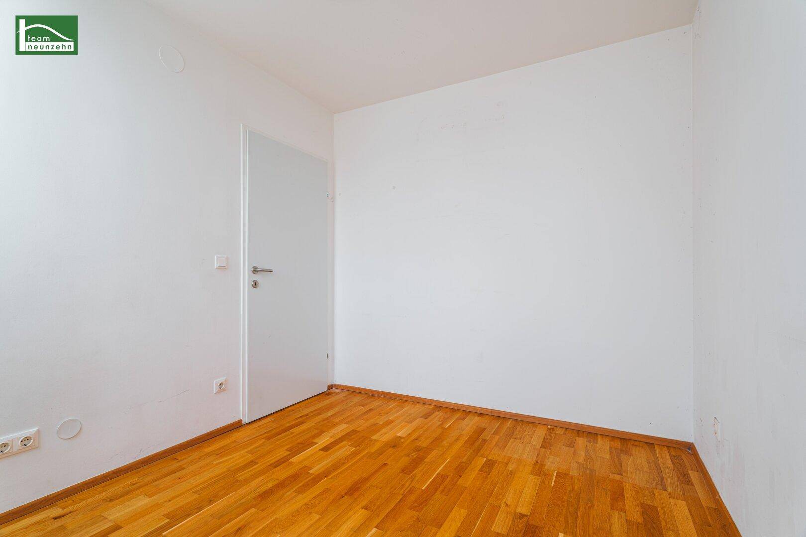 Leeres Zimmer mit hellem Parkettboden und weißen Wänden, ideal als Schlaf- oder Arbeitszimmer.