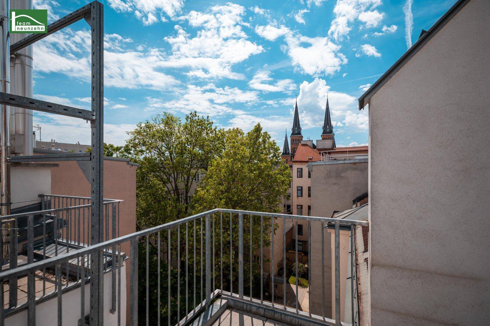Balkon mit Blick auf grüne Bäume und die Kirchtürme der Stadt, bietet eine ruhige Aussicht.