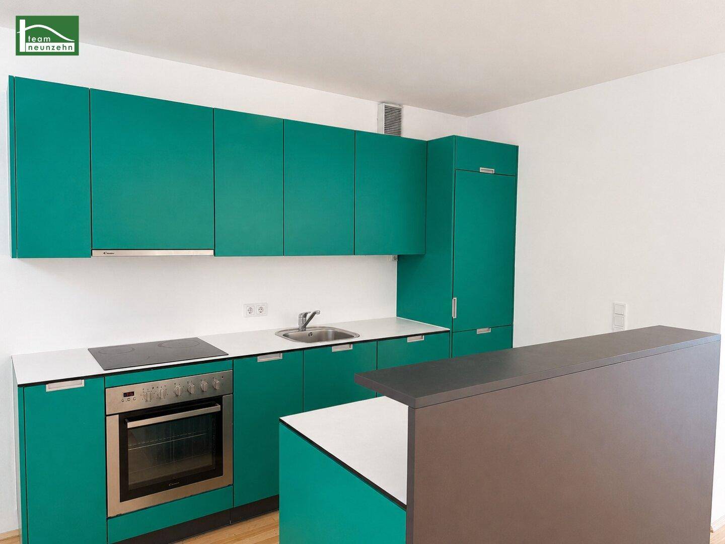 Moderne Einbauküche in leuchtendem Türkis mit Induktionskochfeld und integriertem Backofen.