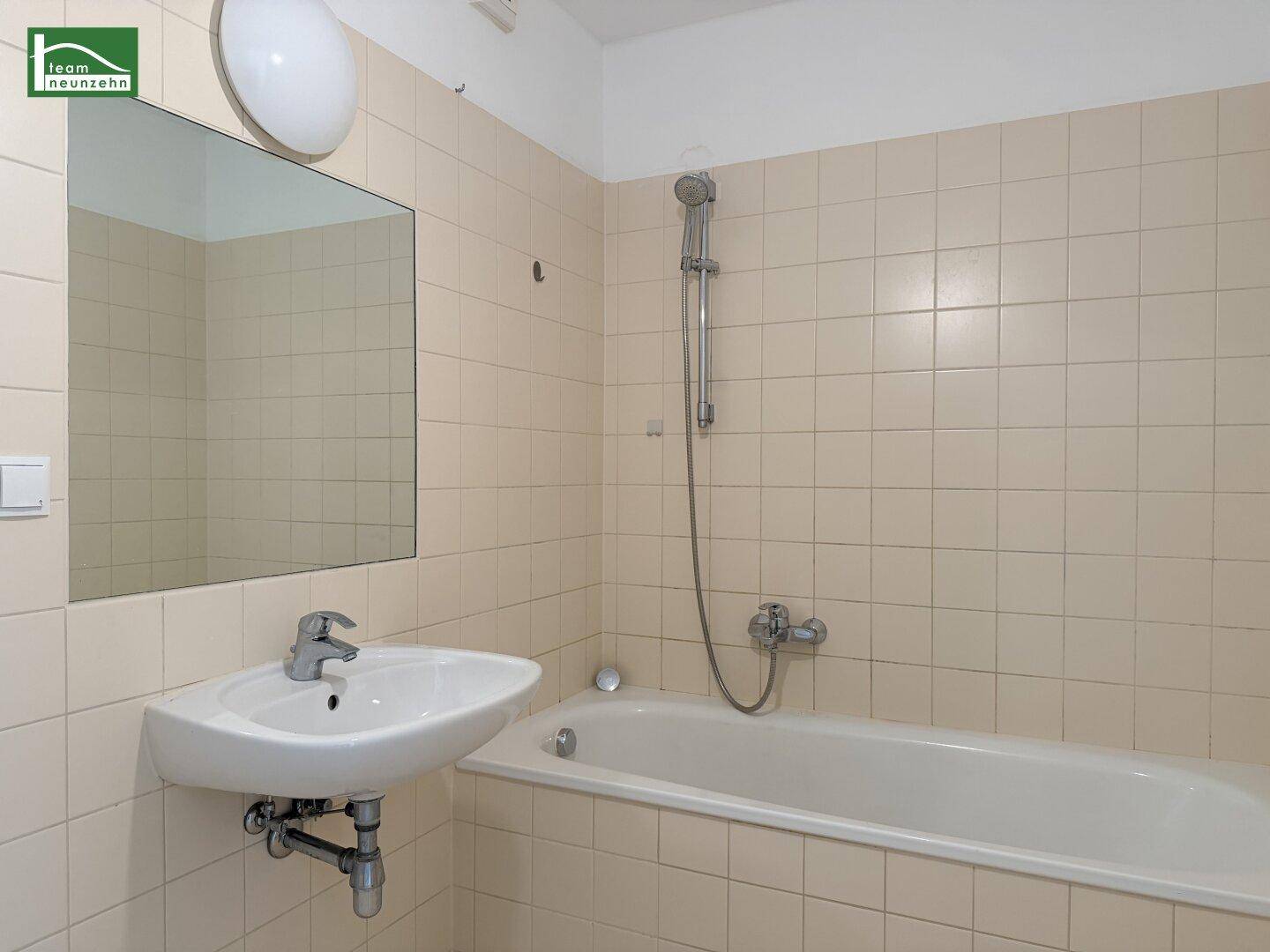 Funktionales Badezimmer mit beigefarbenen Fliesen, Badewanne mit Duschfunktion und Waschbecken.