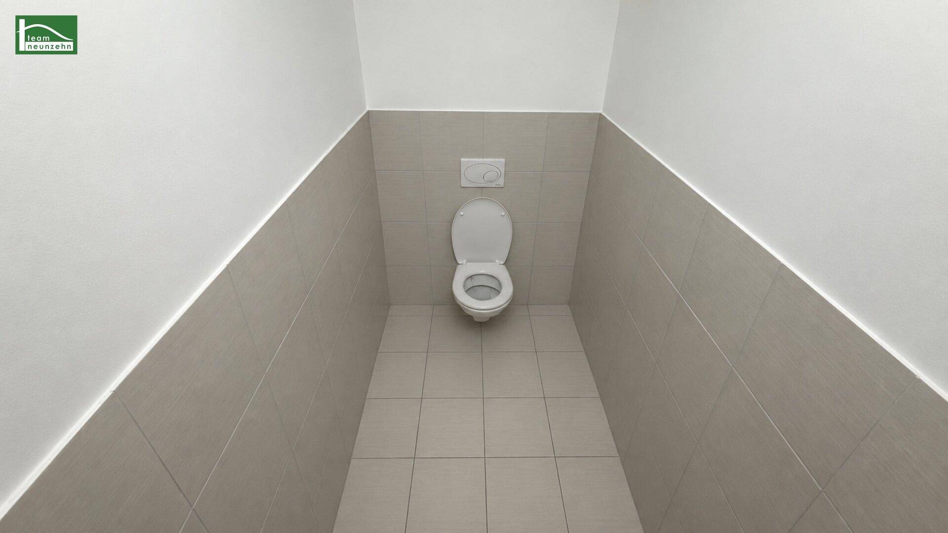 Modernes Gäste-WC mit Wand-WC und hellen Fliesen an Wänden und Boden.