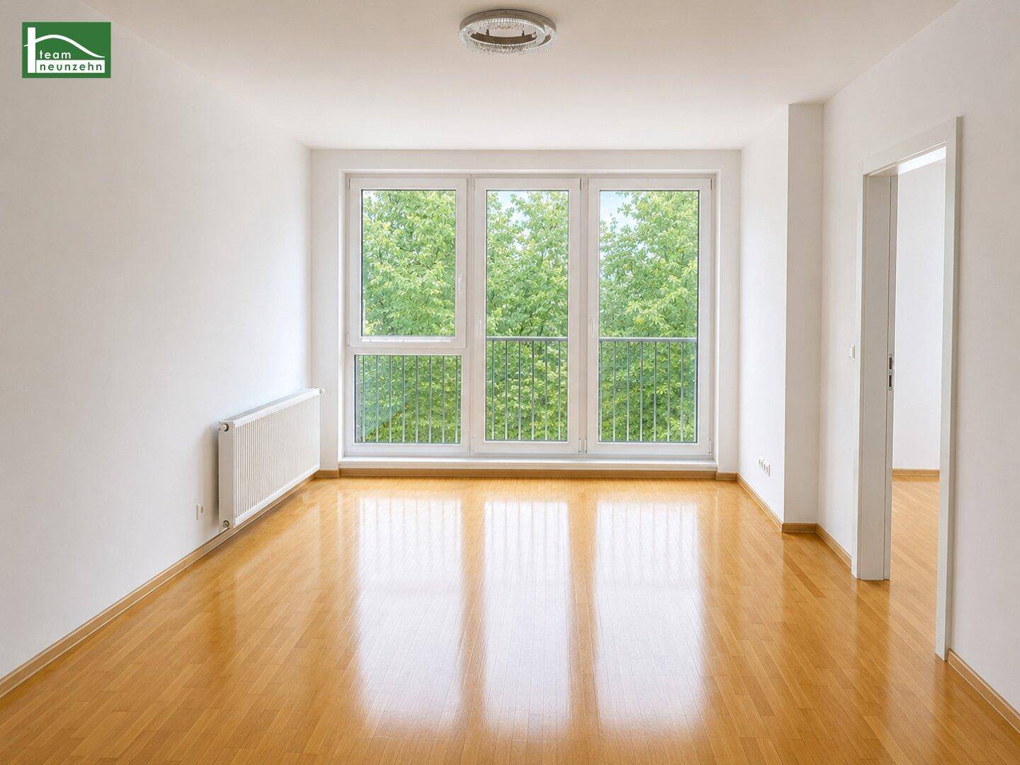 Helles, leeres Zimmer mit großen Fenstern, Holzboden und Blick ins Grüne.