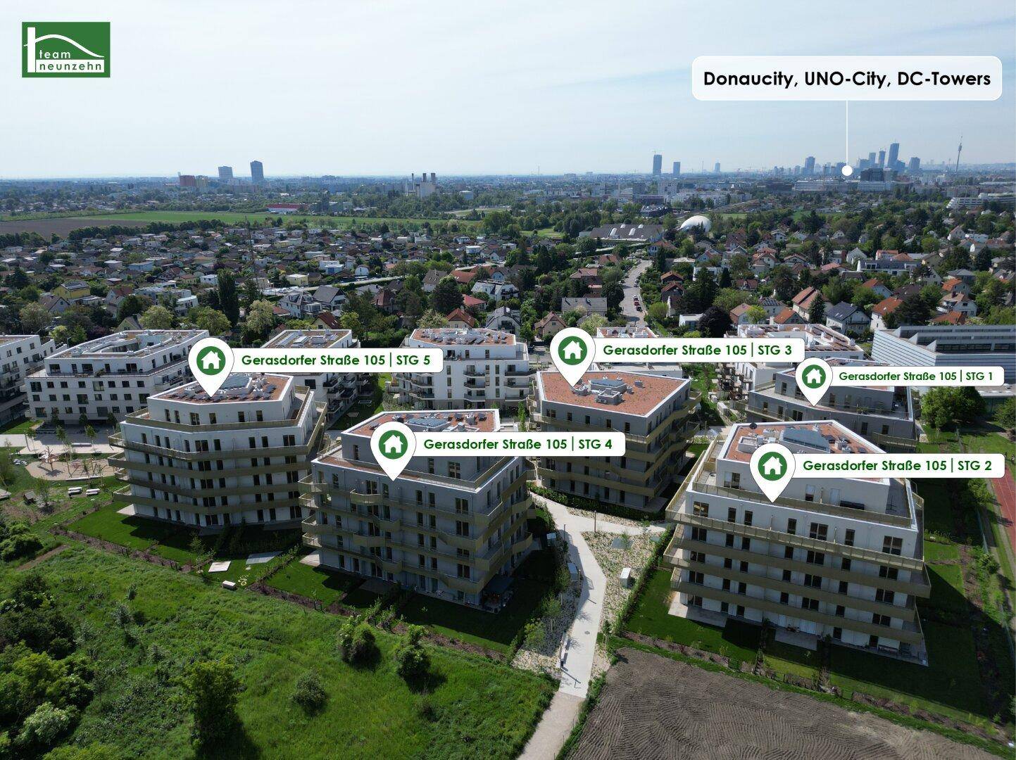 Luftaufnahme moderner Wohngebäude mit Flachdächern, umgeben von Grünflächen und Blick auf die Stadt.
