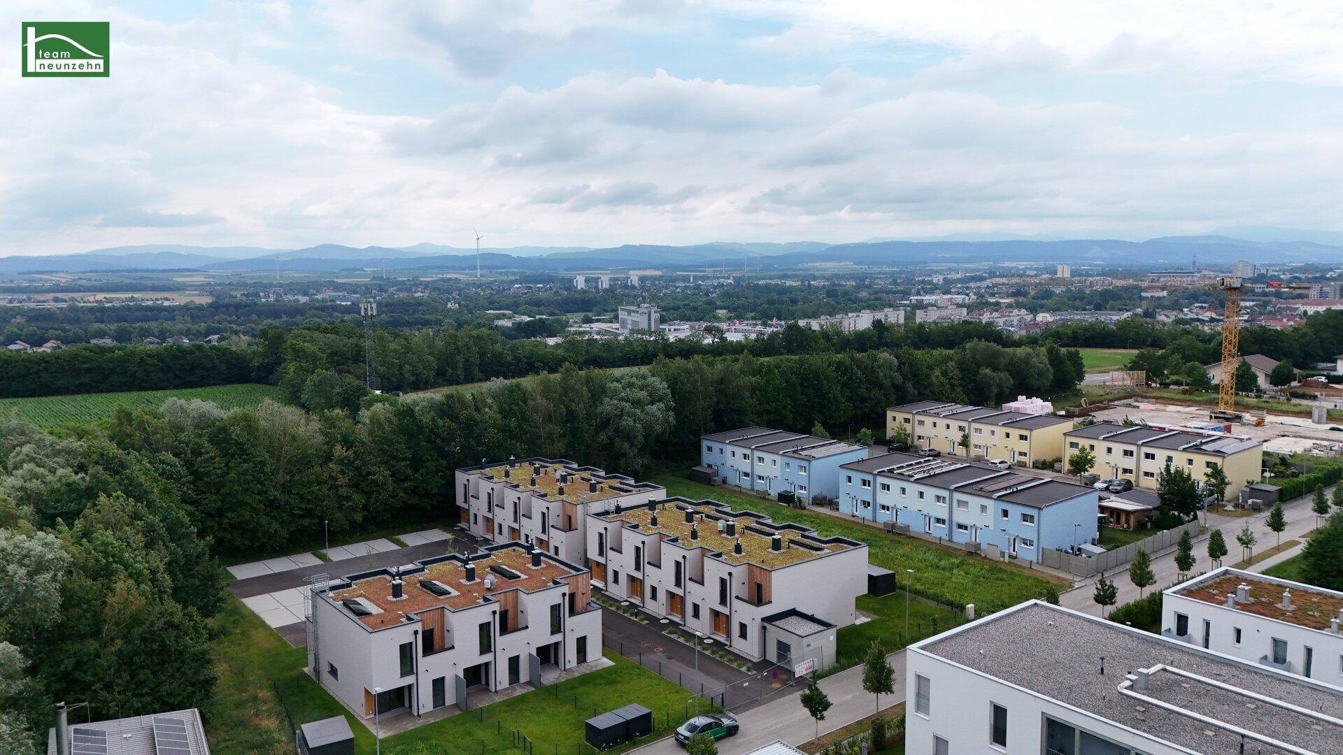 Luftaufnahme einer modernen Wohnsiedlung mit Reihenhäusern und angrenzenden Mehrfamilienhäusern.