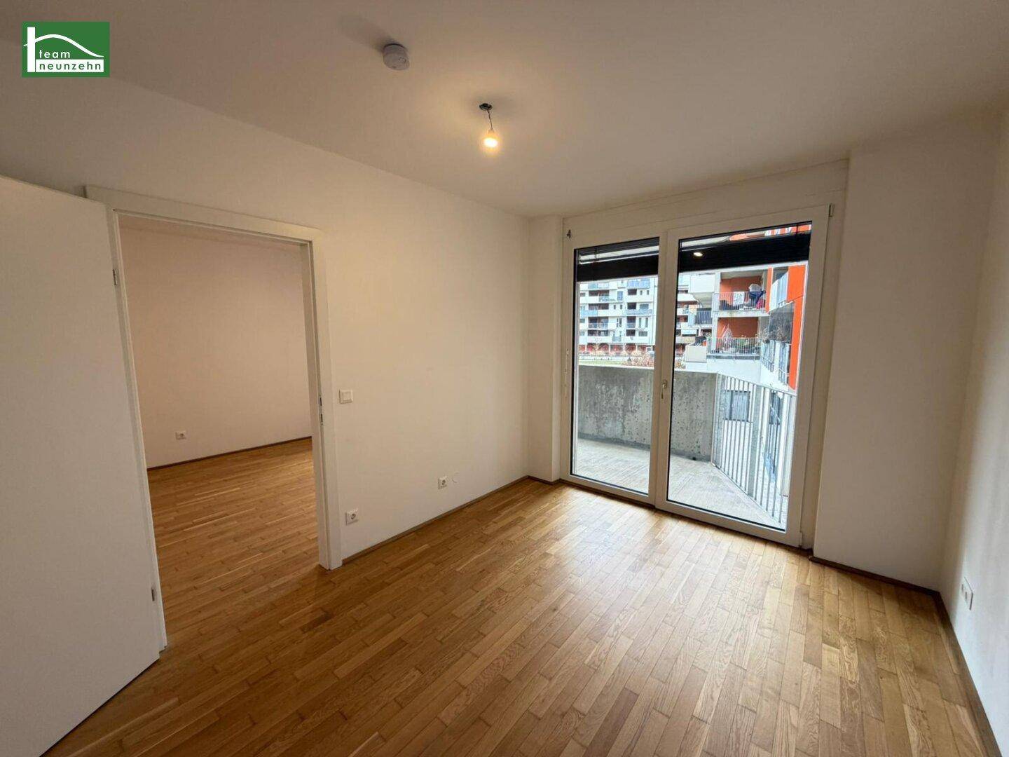 Helles, leeres Schlafzimmer mit Holzboden und direktem Zugang zum Balkon.