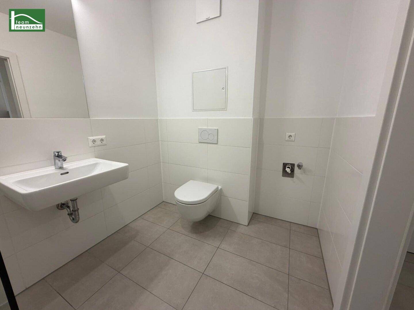 Modernes WC mit wandhängender Toilette, Waschbecken und hellen Fliesen an den Wänden.