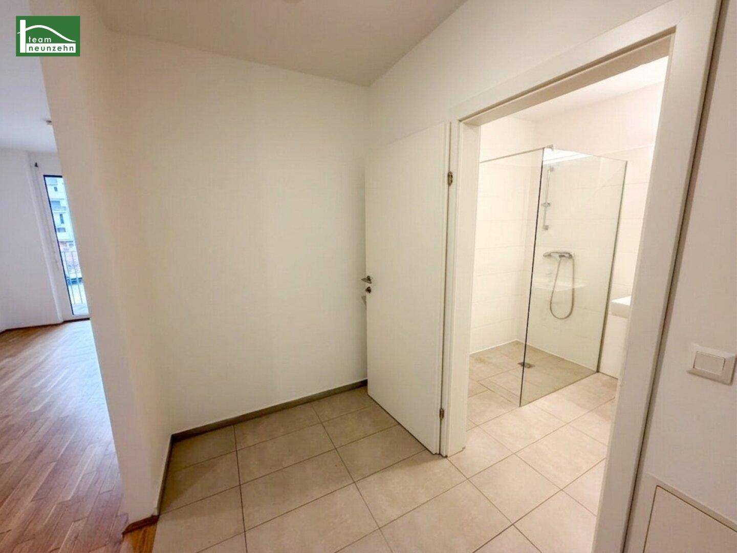 Heller Flur mit Fliesenboden, der zum modernen Badezimmer mit Dusche führt.