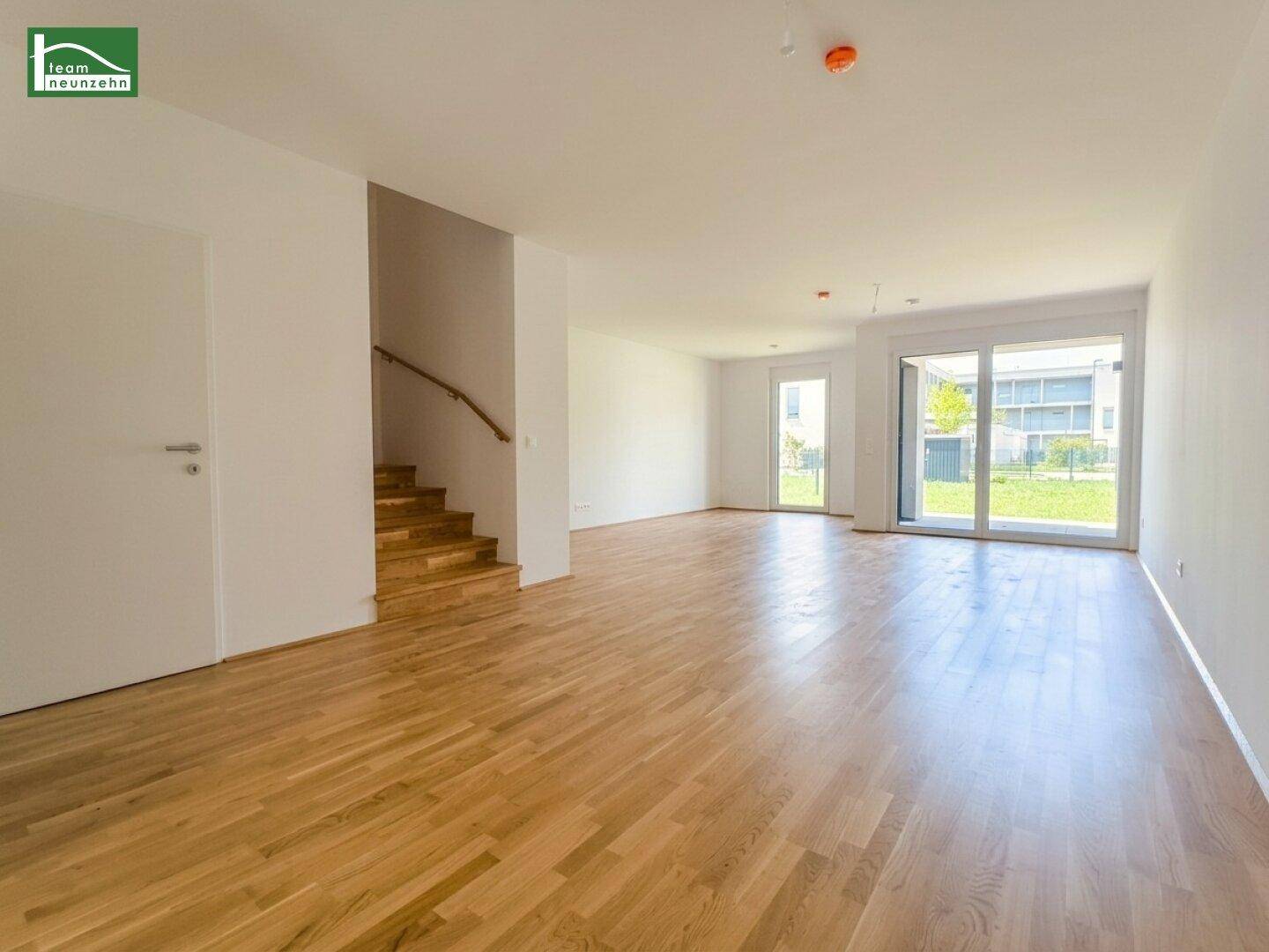 Heller, unmöblierter Wohnbereich mit Holzparkettboden, Treppe und großen Fenstern zum Garten.