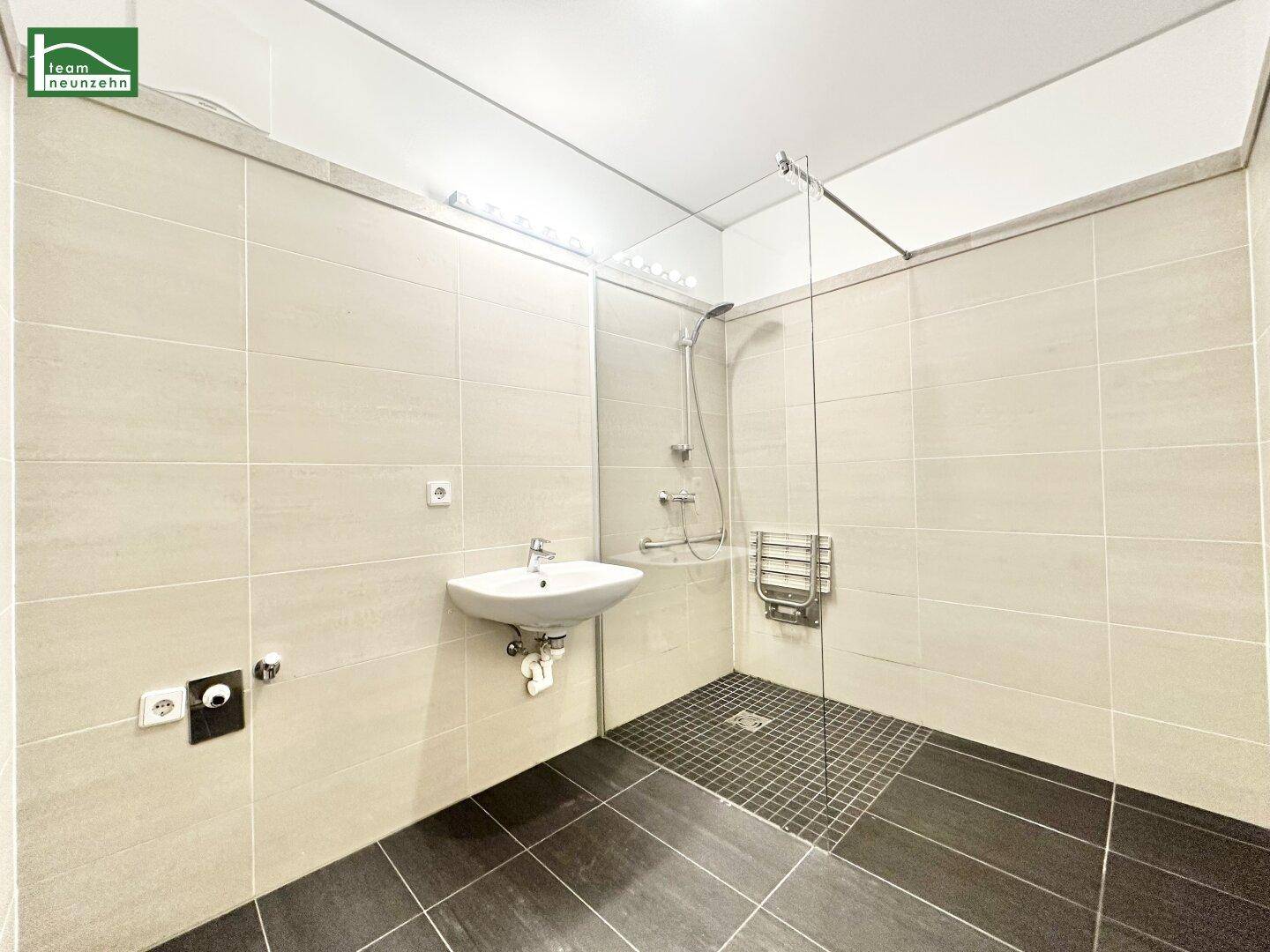 Modernes Badezimmer mit ebenerdiger Dusche, Waschbecken und hellen Fliesen.