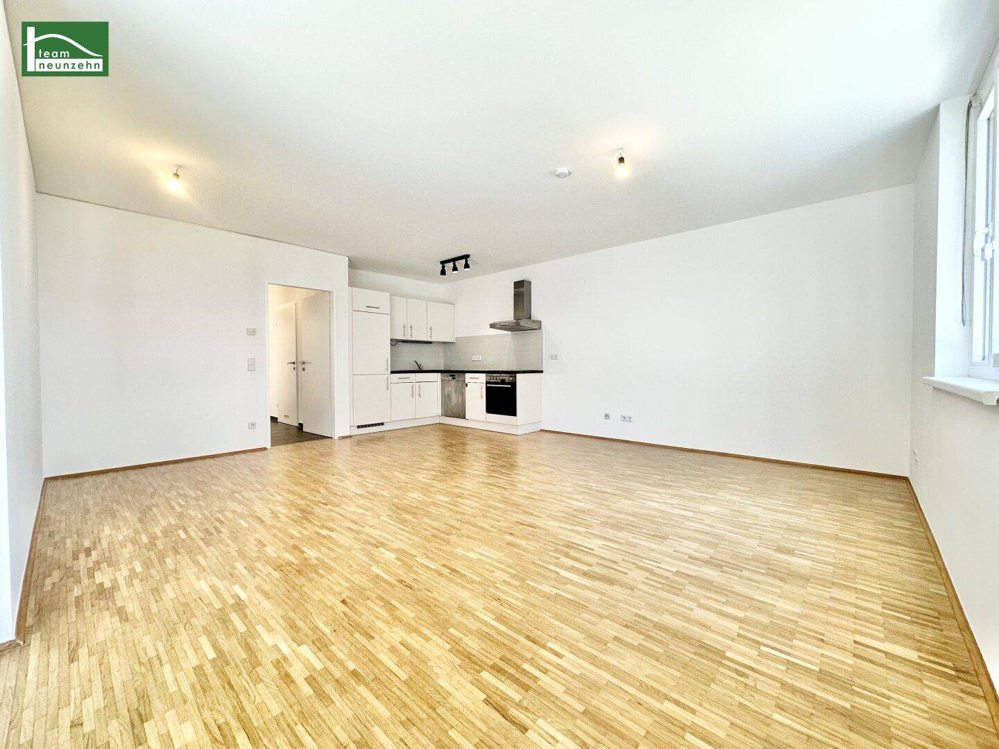 Offener Wohnbereich mit integrierter Küche, Parkettboden und viel Tageslicht.