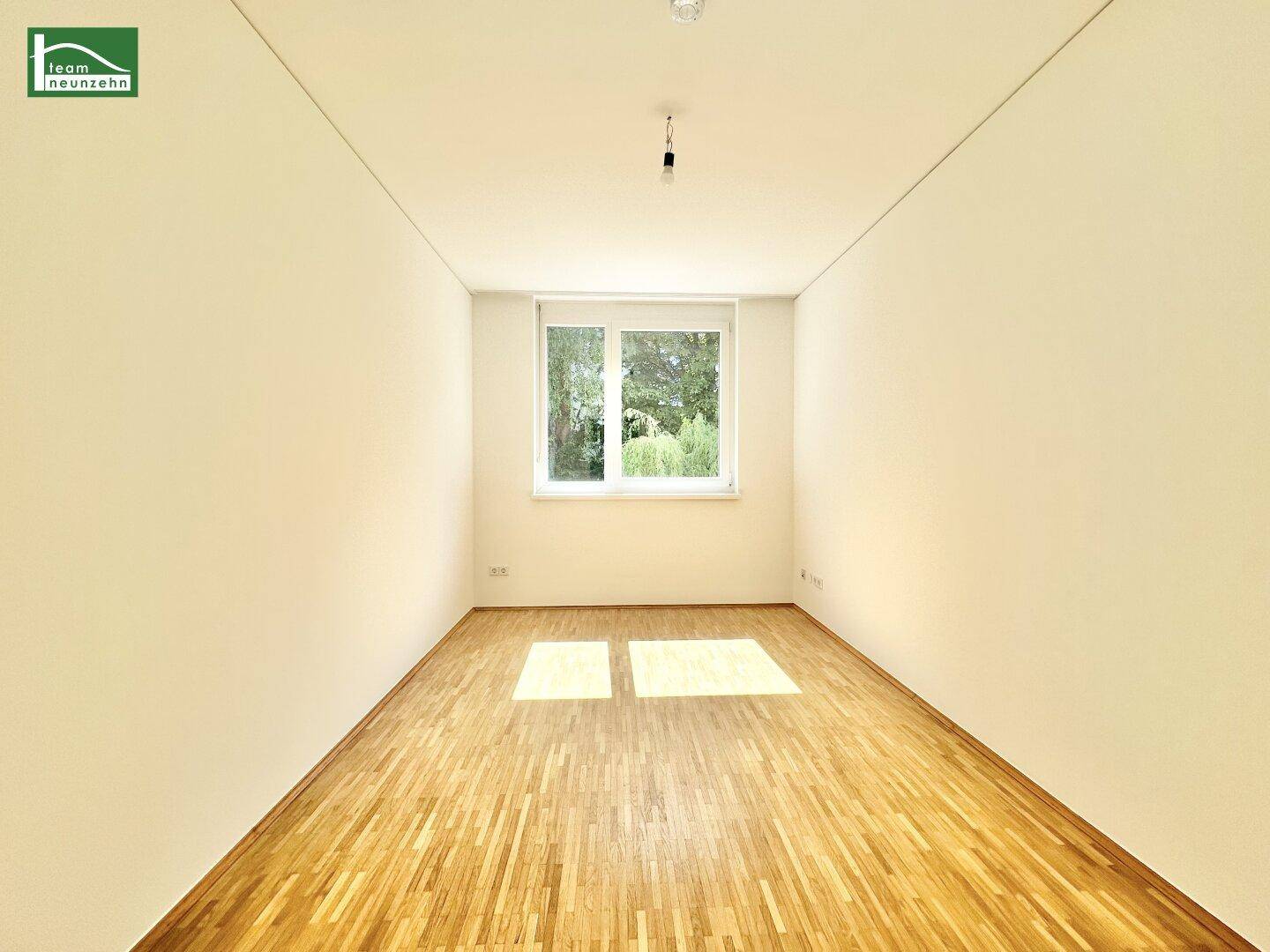 Helles Zimmer mit Parkettboden und großem Fenster, das viel Tageslicht hereinlässt.