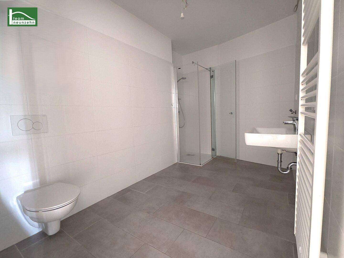 Modernes Badezimmer mit grauen Fliesen, wandhängendem WC und ebenerdiger Dusche.