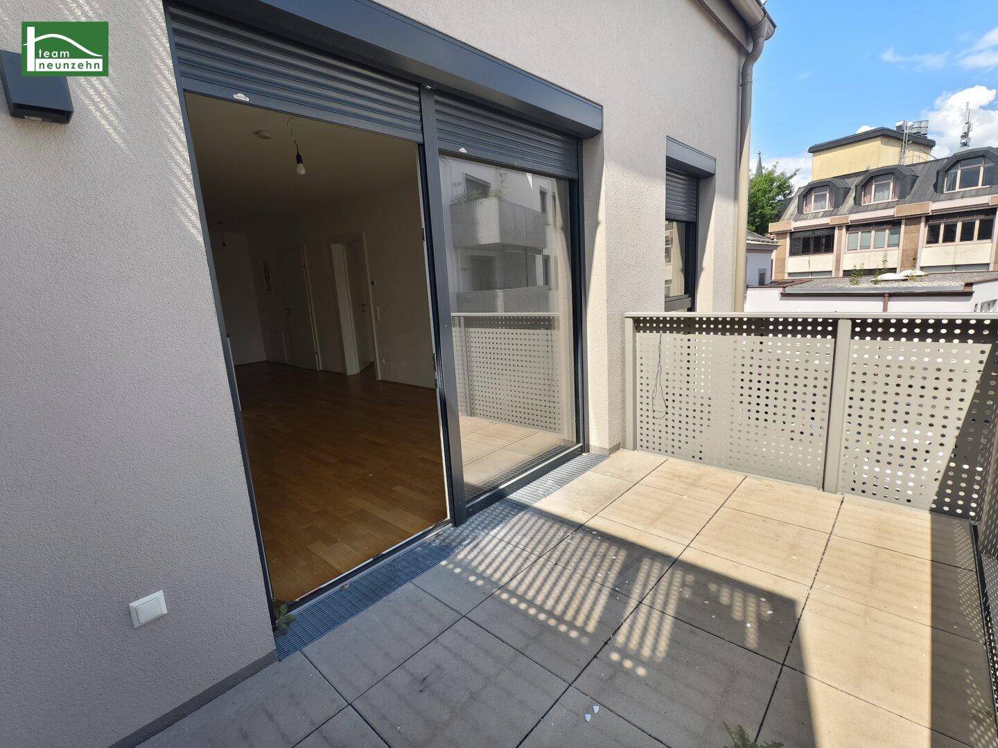 Sonniger Balkon mit Zugang zum Innenraum und Blick auf die Nachbarschaft.