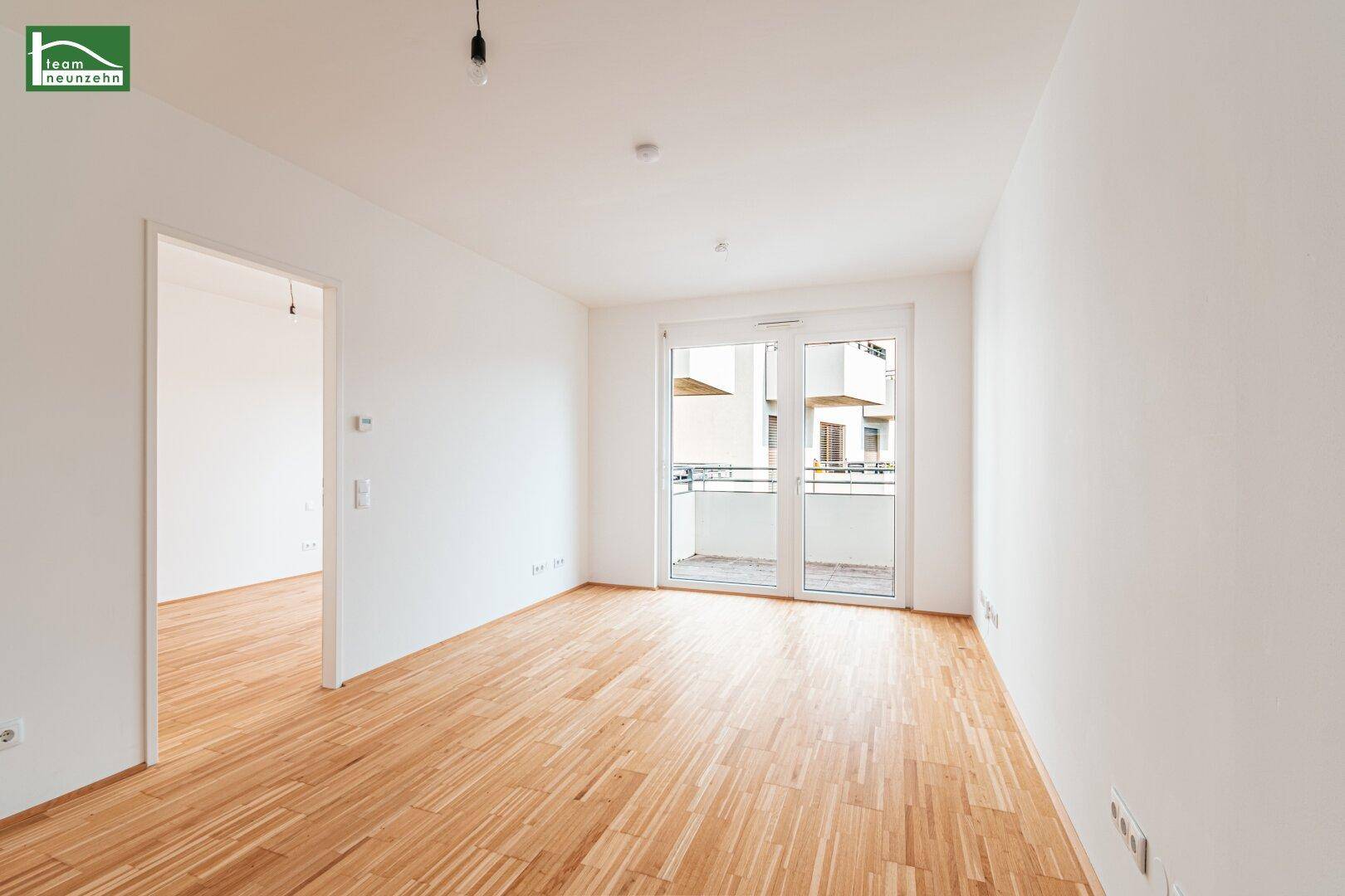 Heller Wohnraum mit Zugang zu einem Balkon und hellem Parkettboden.