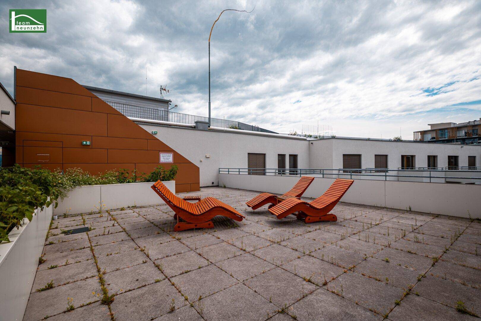 Weitläufige Dachterrasse mit Liegestühlen und Blick auf die Stadt und Berge.