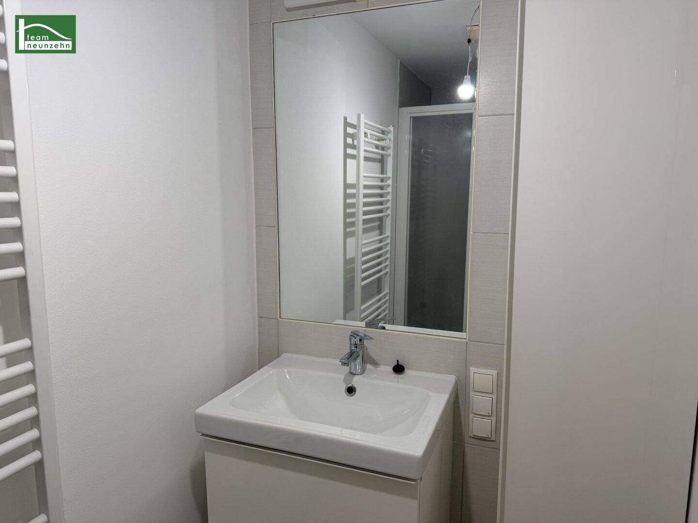 Modernes Badezimmer mit Waschbecken, Spiegel und Duschkabine, ausgestattet mit einem Handtuchheizkörper.