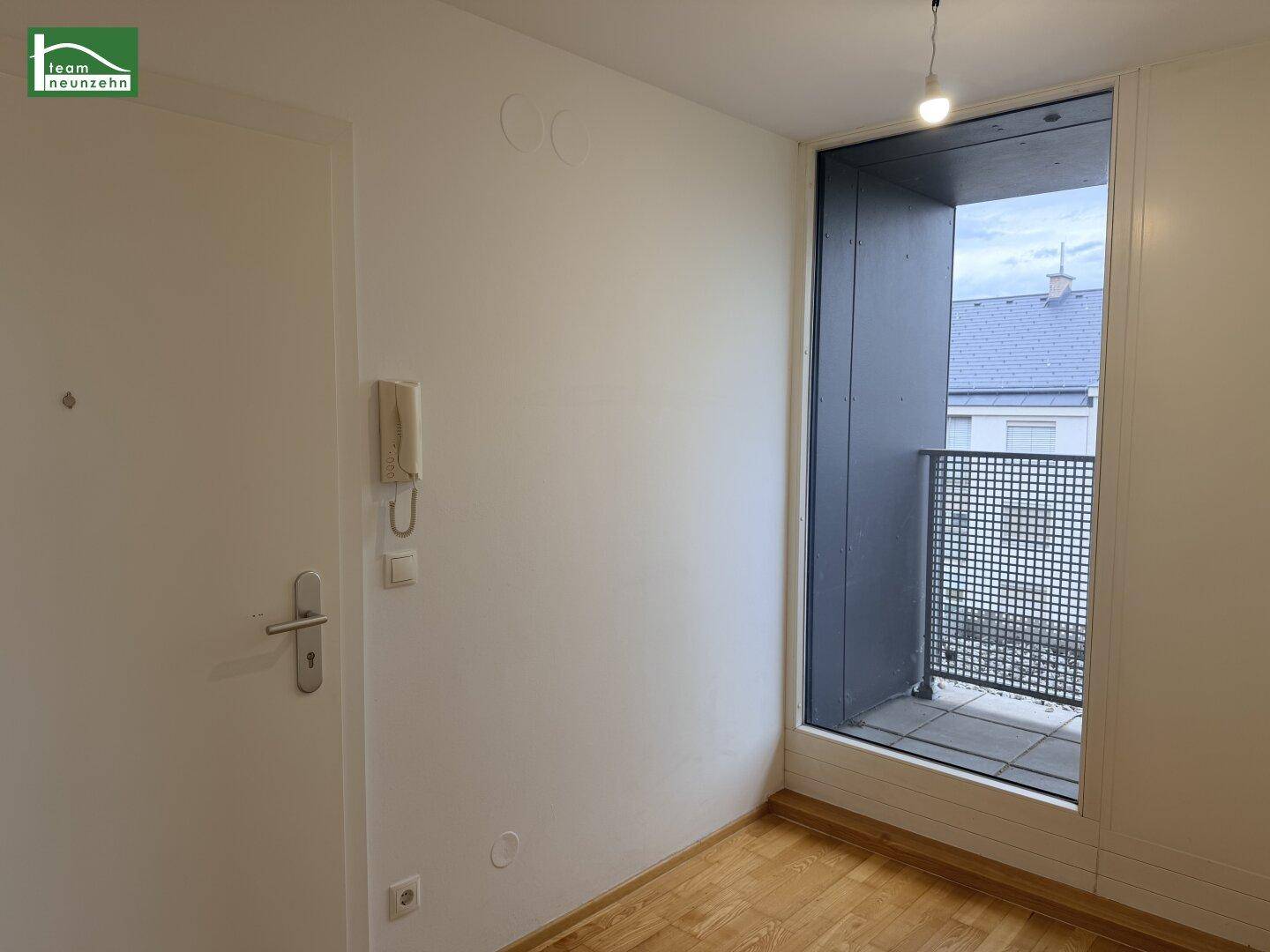 Heller Flur mit Holzboden und Zugang zu einem kleinen Balkon, der Tageslicht hereinlässt.