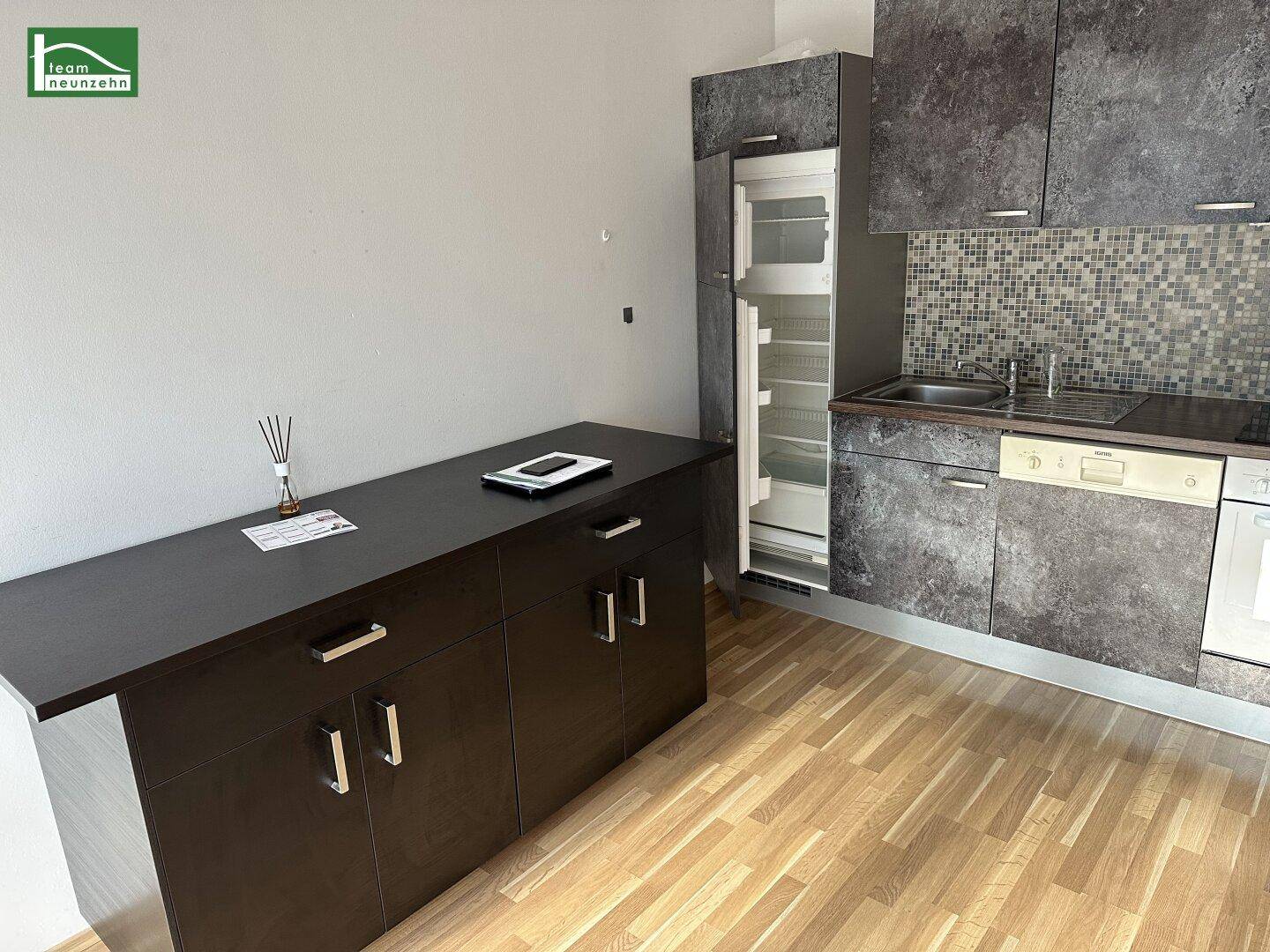Funktionale Küche mit dunklen Schränken, integriertem Kühlschrank und hellem Holzfußboden.