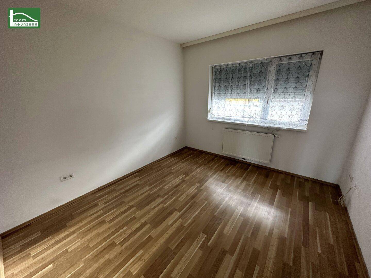 Helles Schlafzimmer mit Holzparkettboden und einem Fenster mit Rollladen, bereit zur Einrichtung.