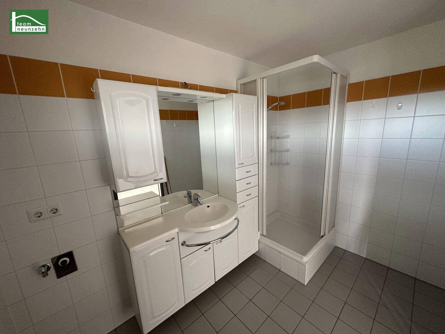 Badezimmer mit weißem Waschtischunterschrank, Spiegel und einer Duschkabine, gefliest in Weiß und Orange.