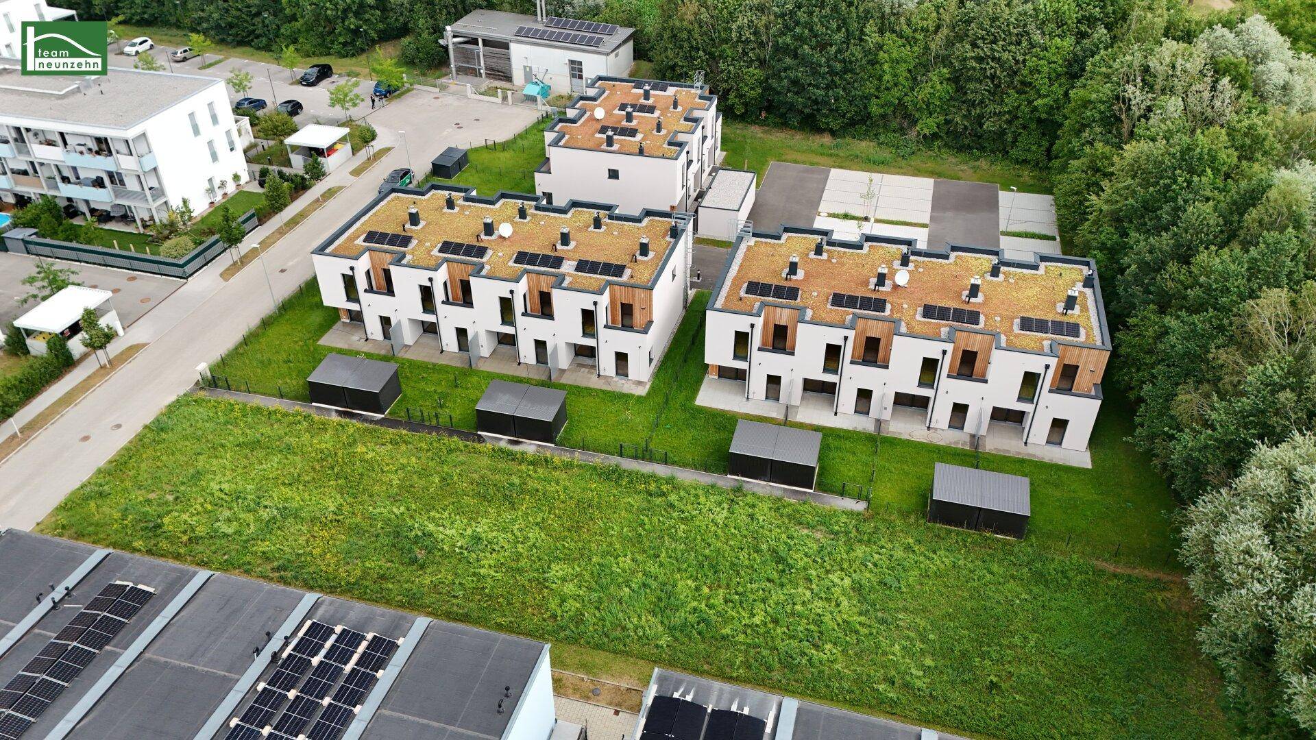 Luftaufnahme einer modernen Wohnanlage mit Gründächern, Solaranlagen und umliegenden Grünflächen.
