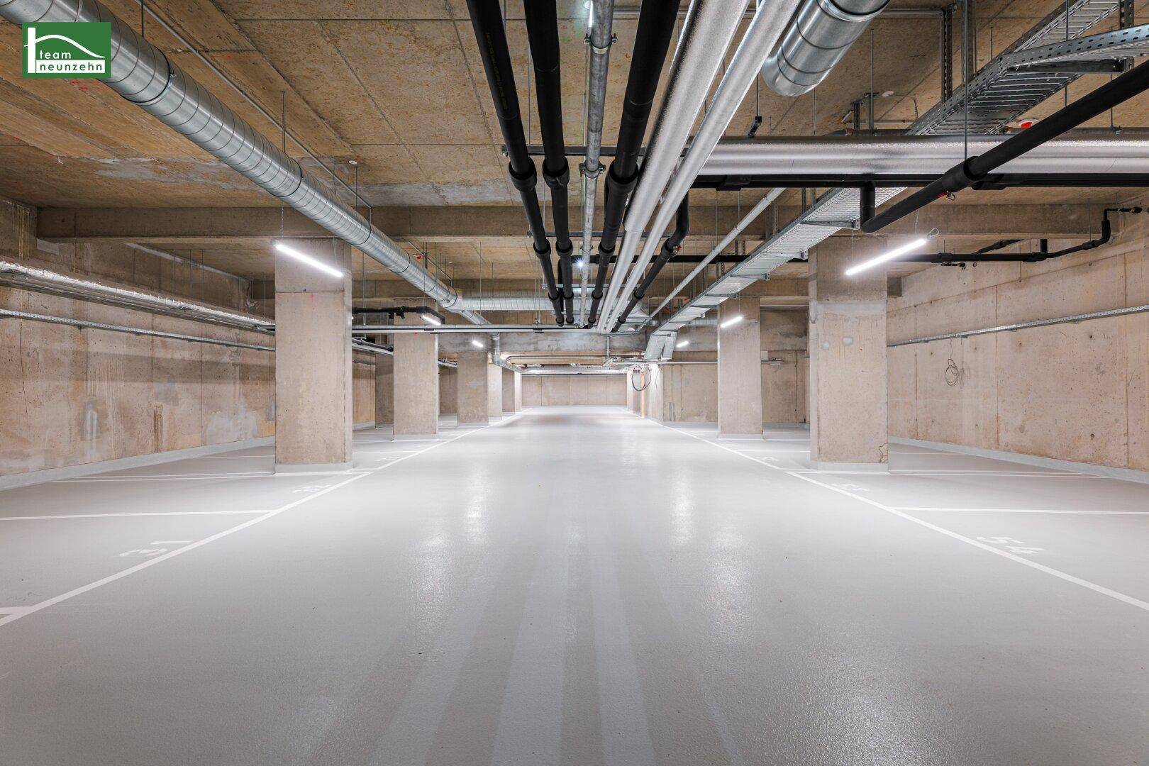 Geräumige Tiefgarage mit markierten Stellplätzen und sichtbaren Leitungen an der Decke.
