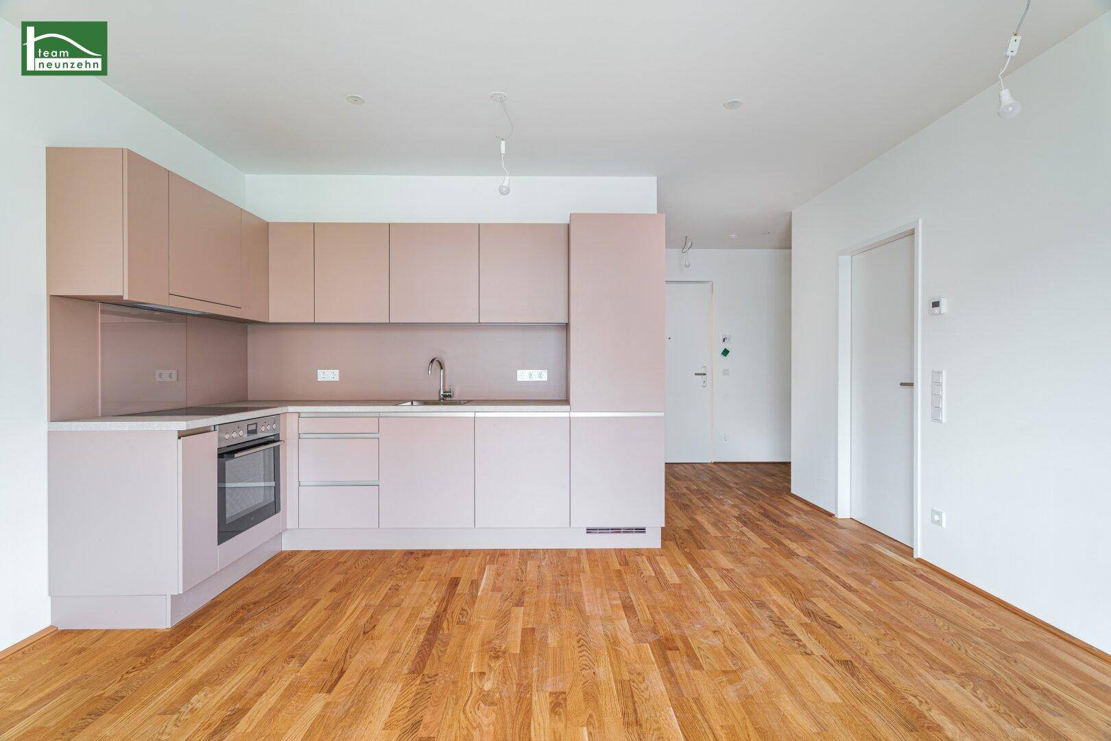 Moderne Einbauküche in hellem Roséton mit integriertem Backofen und Holzboden in offenem Wohnbereich.