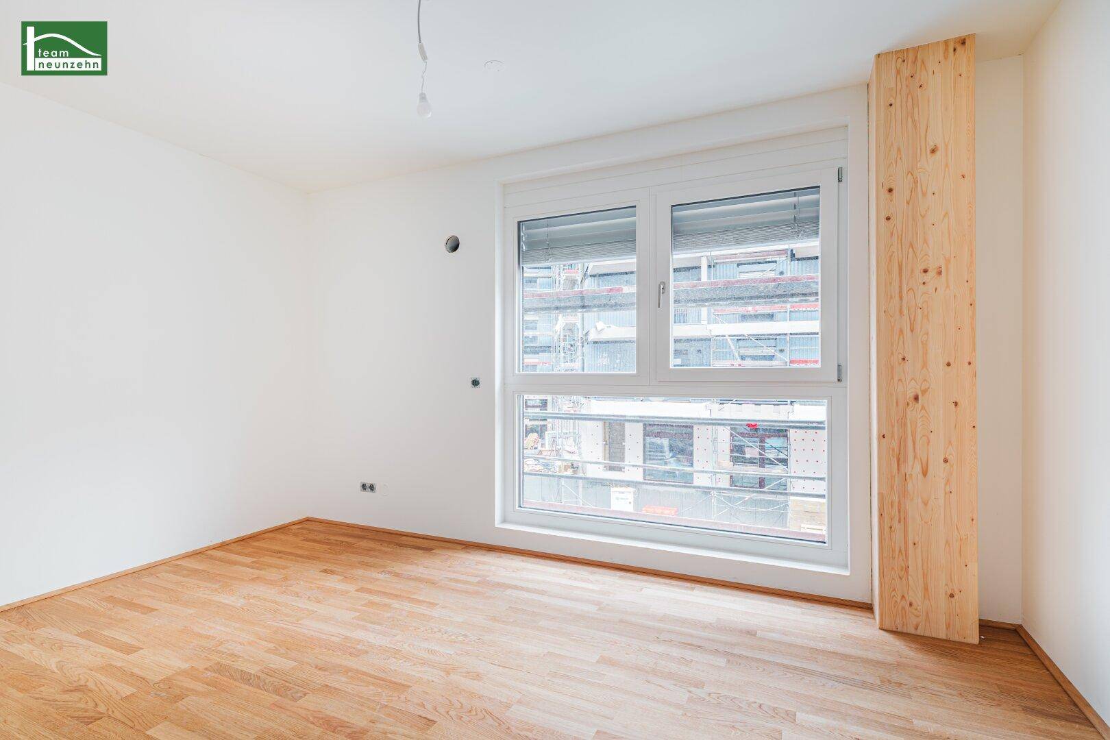 Helles, unmöbliertes Zimmer mit Holzboden und einem großen Fenster, das viel Tageslicht hereinlässt.