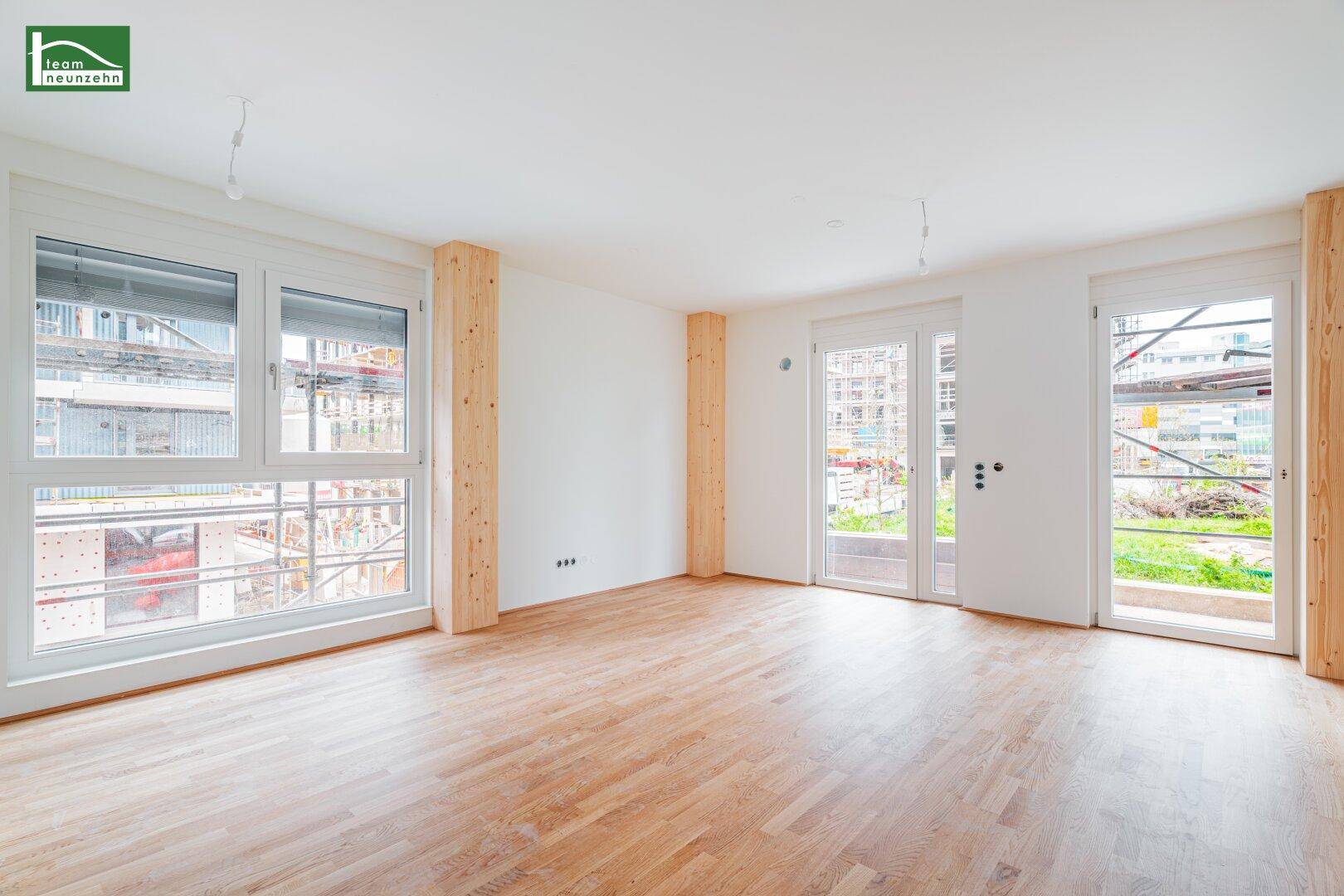Helles, leeres Zimmer mit Holzboden und großen Fenstern, bereit für die individuelle Gestaltung.