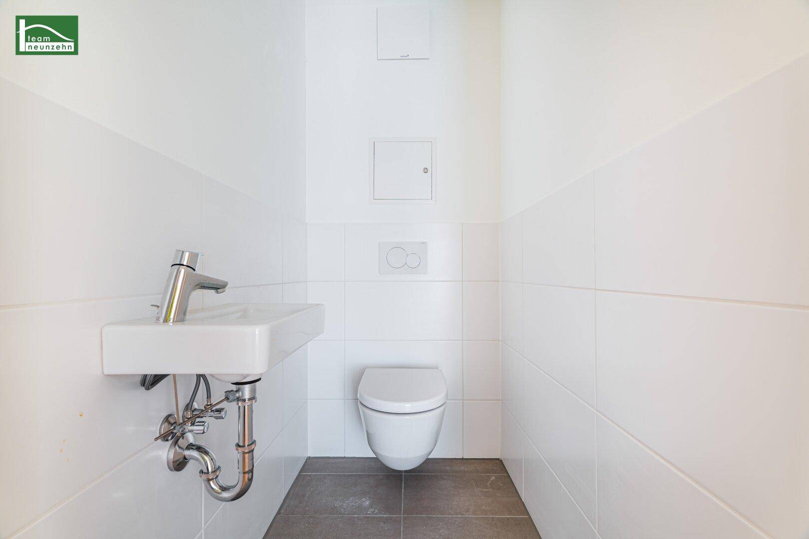 Separates Gäste-WC mit wandmontierter Toilette, kleinem Waschbecken und weißen Fliesen.