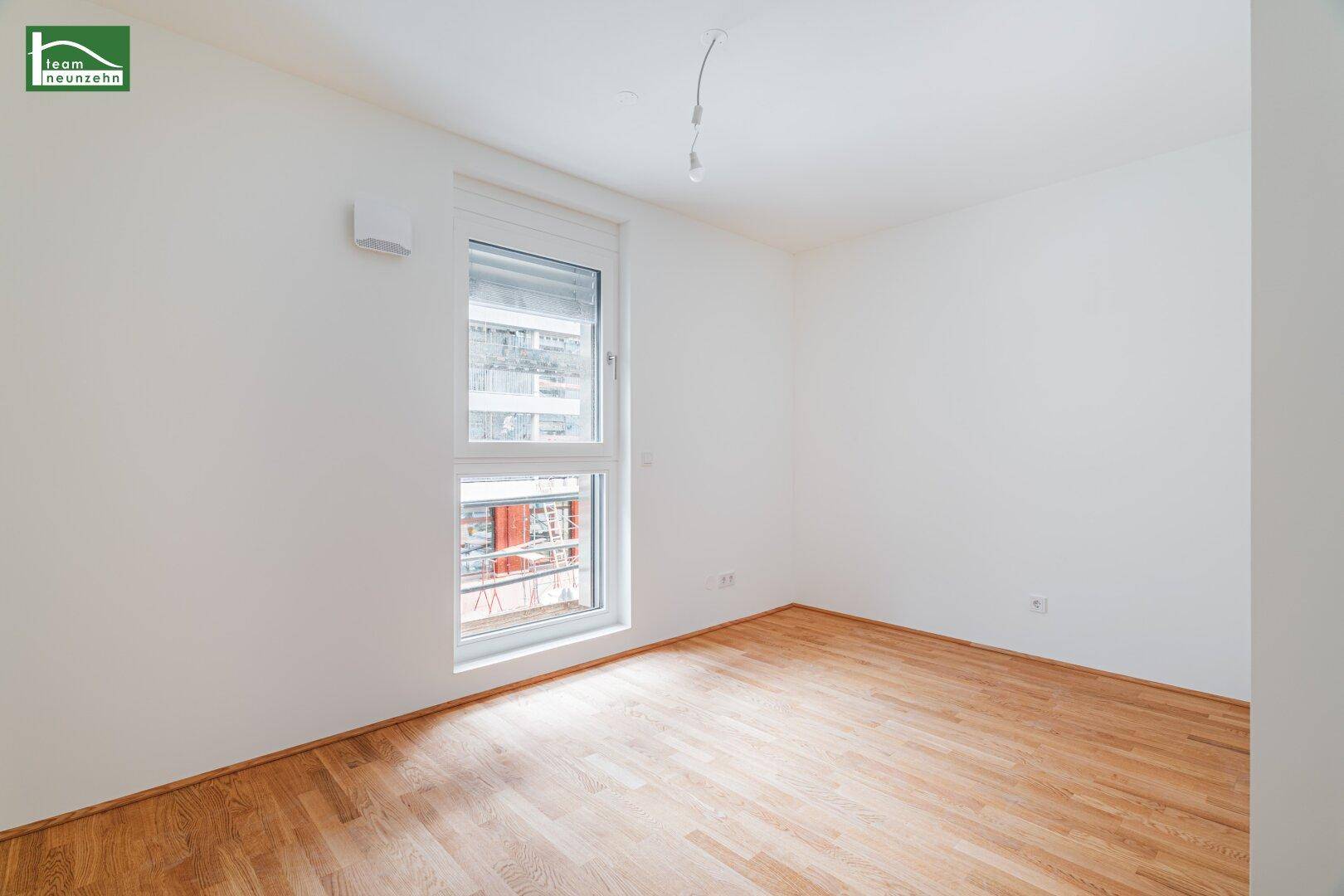 Heller, unmöblierter Raum mit Holzboden und einem Fenster, das viel Tageslicht hereinlässt.