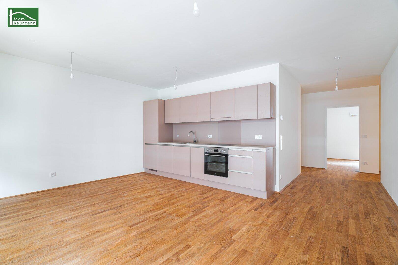 Offene Küche mit modernen, hellrosa Schränken und Holzboden in einem hellen Wohnbereich.