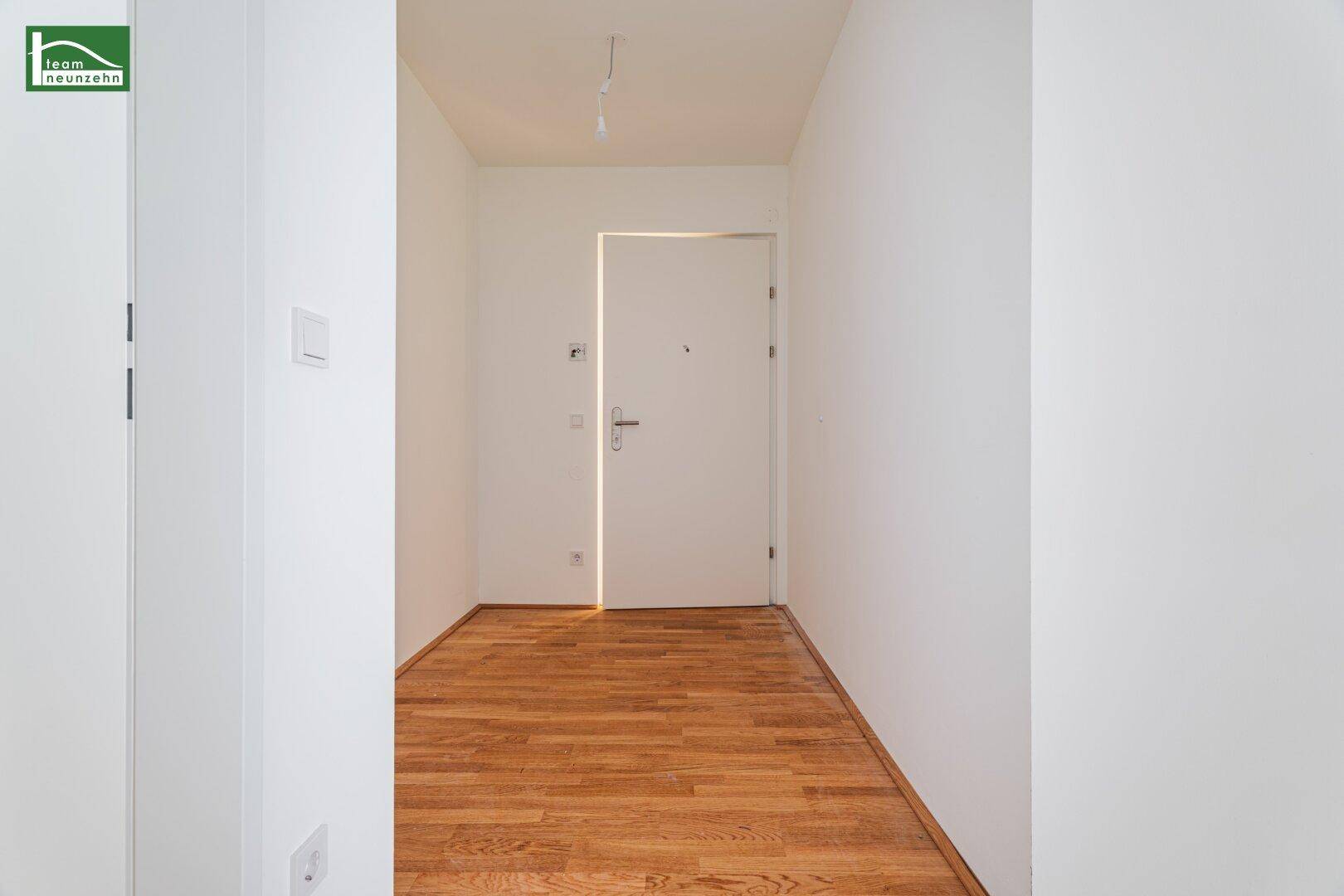 Heller Eingangsbereich mit Holzboden und weißer Tür, führt in die moderne Wohnung.