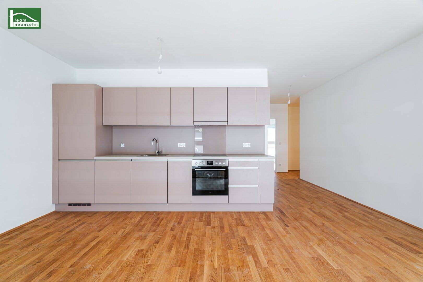 Moderne Einbauküche in hellem Beige mit integriertem Backofen und Holzboden in einem offenen Wohnbereich.