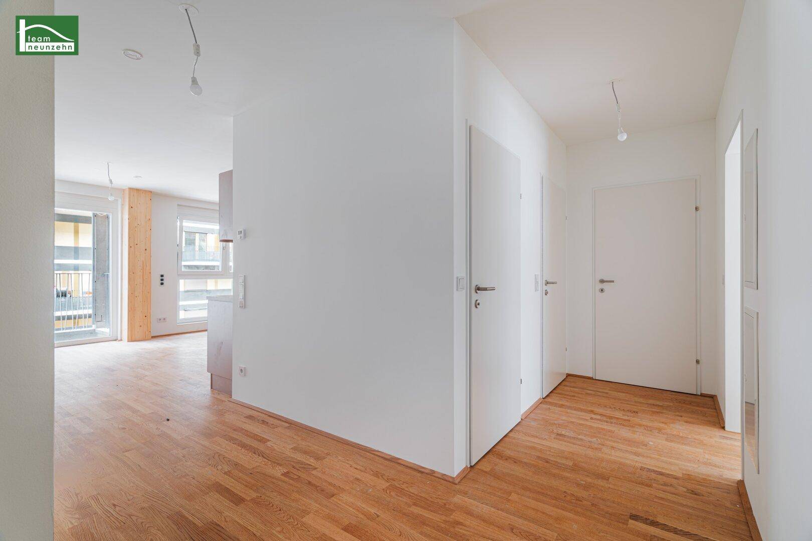 Heller Flur mit Holzboden und weißen Türen, der in einen offenen Wohnbereich führt.