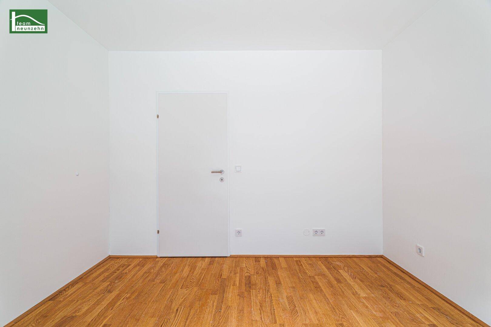 Schlichter Raum mit Holzboden und weißer Tür, bereit zur individuellen Gestaltung.