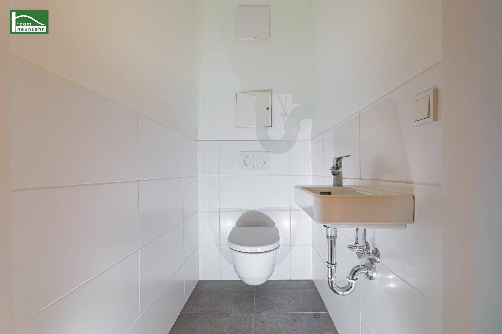 Separates Gäste-WC mit wandhängender Toilette, kleinem Waschbecken und weißen Fliesen.