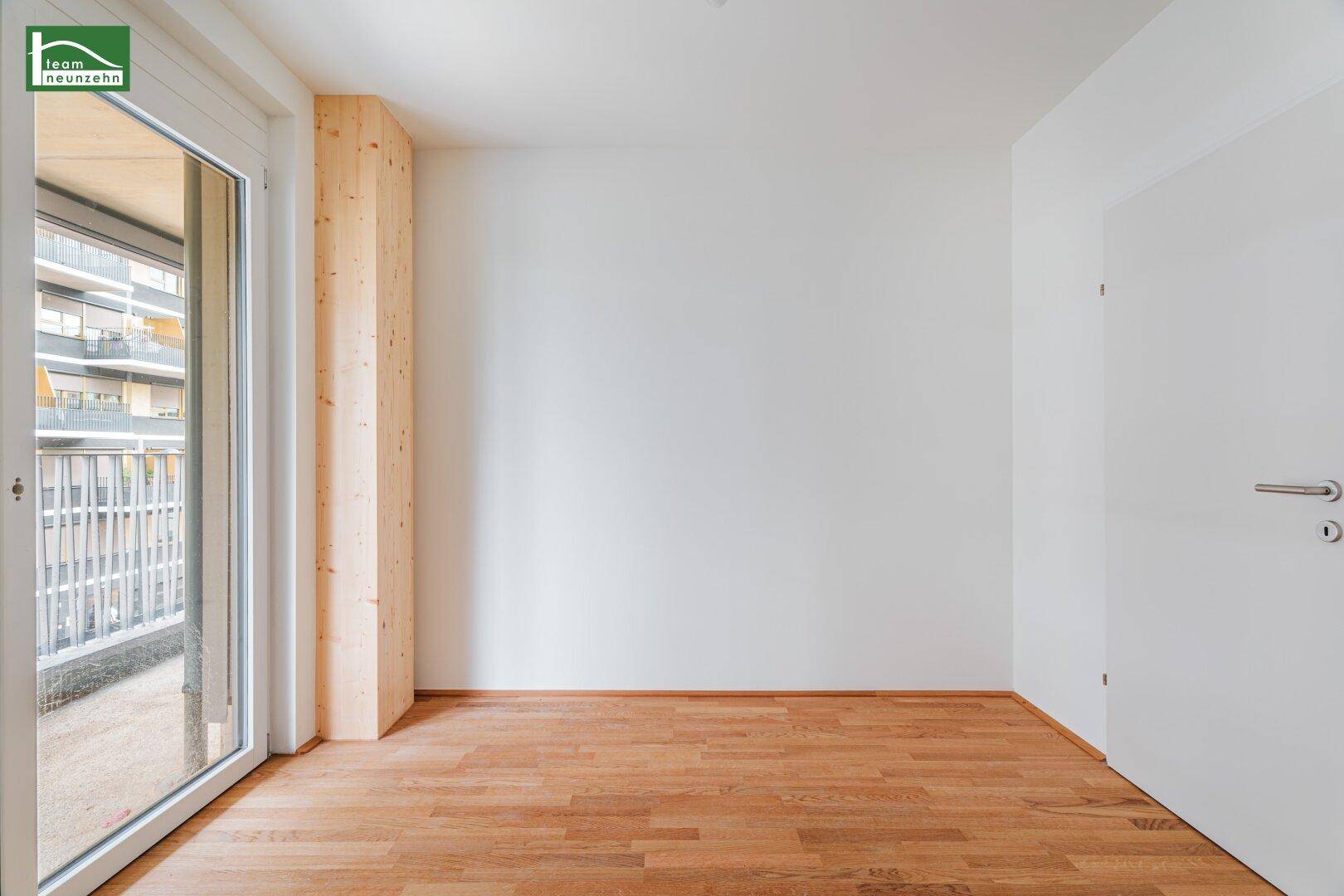 Lichtdurchfluteter Raum mit Holzboden und breitem Balkonzugang, der einen Blick auf die Umgebung freigibt.