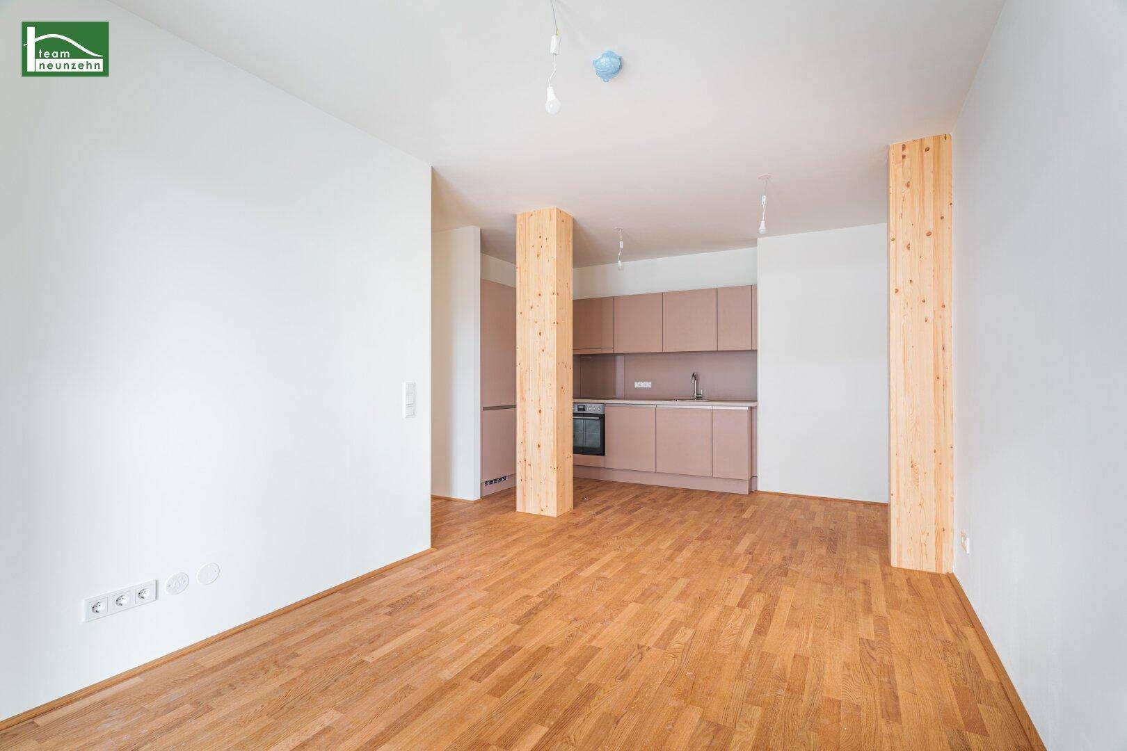 Heller offener Wohnbereich mit integrierter Küche, Holzboden und modernen hellrosa Schränken.