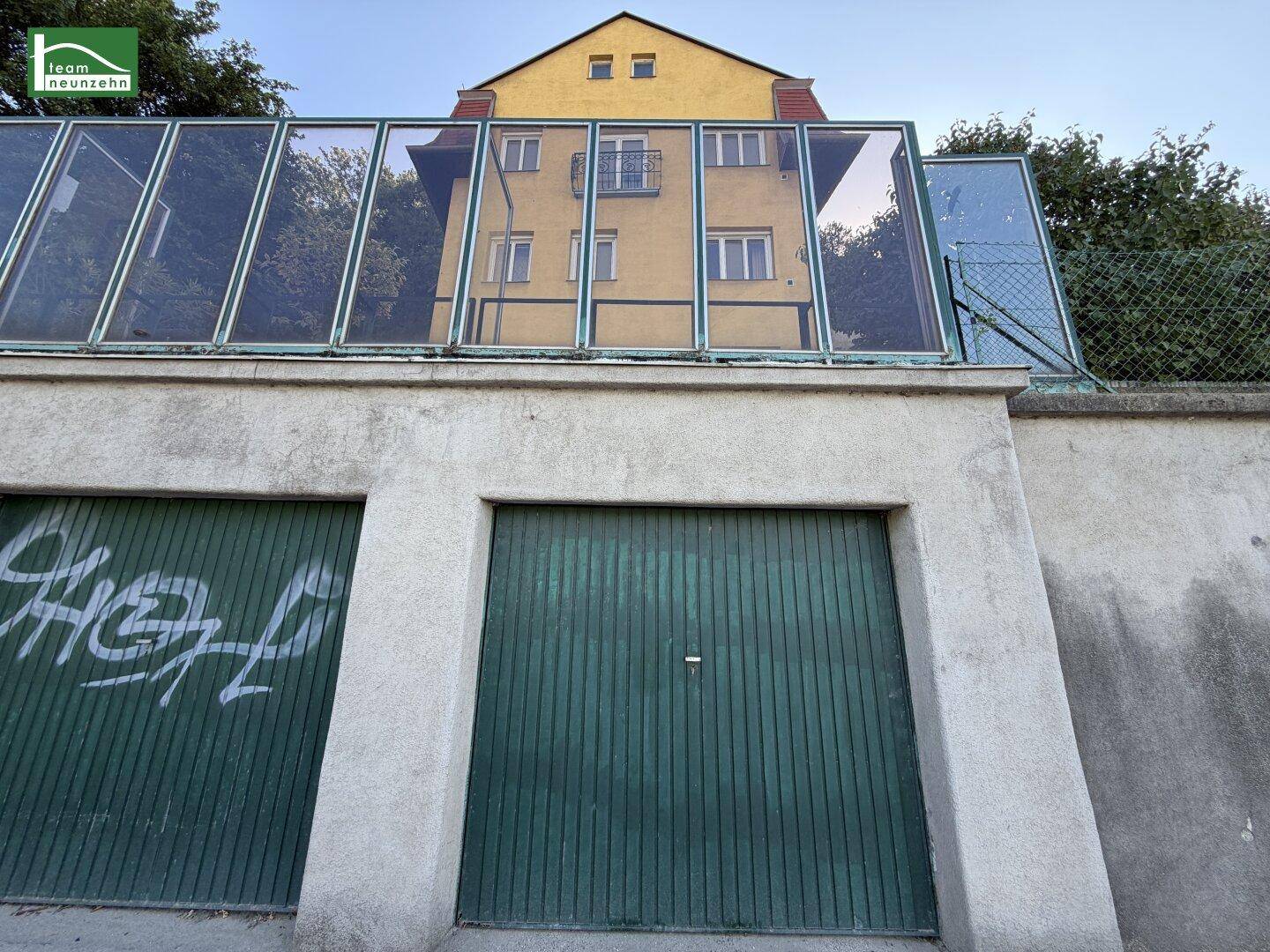 Zwei Garagentore mit Graffiti und einer darüberliegenden Glasüberdachung vor einem gelben Gebäude.