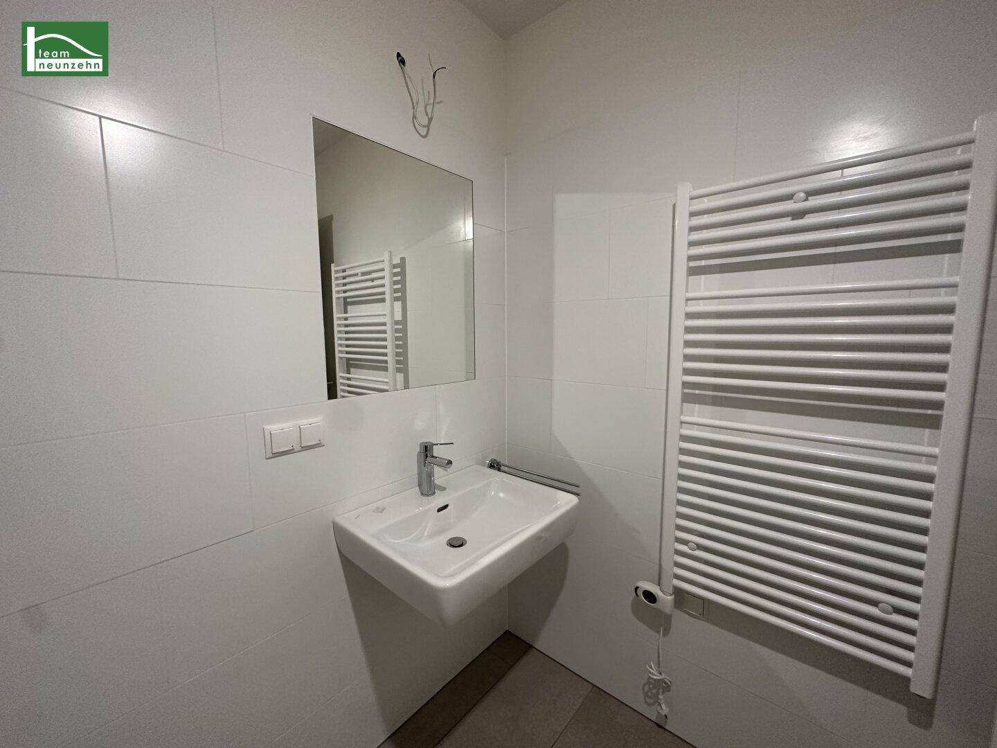 Modernes Badezimmer mit Waschbecken, Spiegel und einem praktischen beheizten Handtuchhalter.