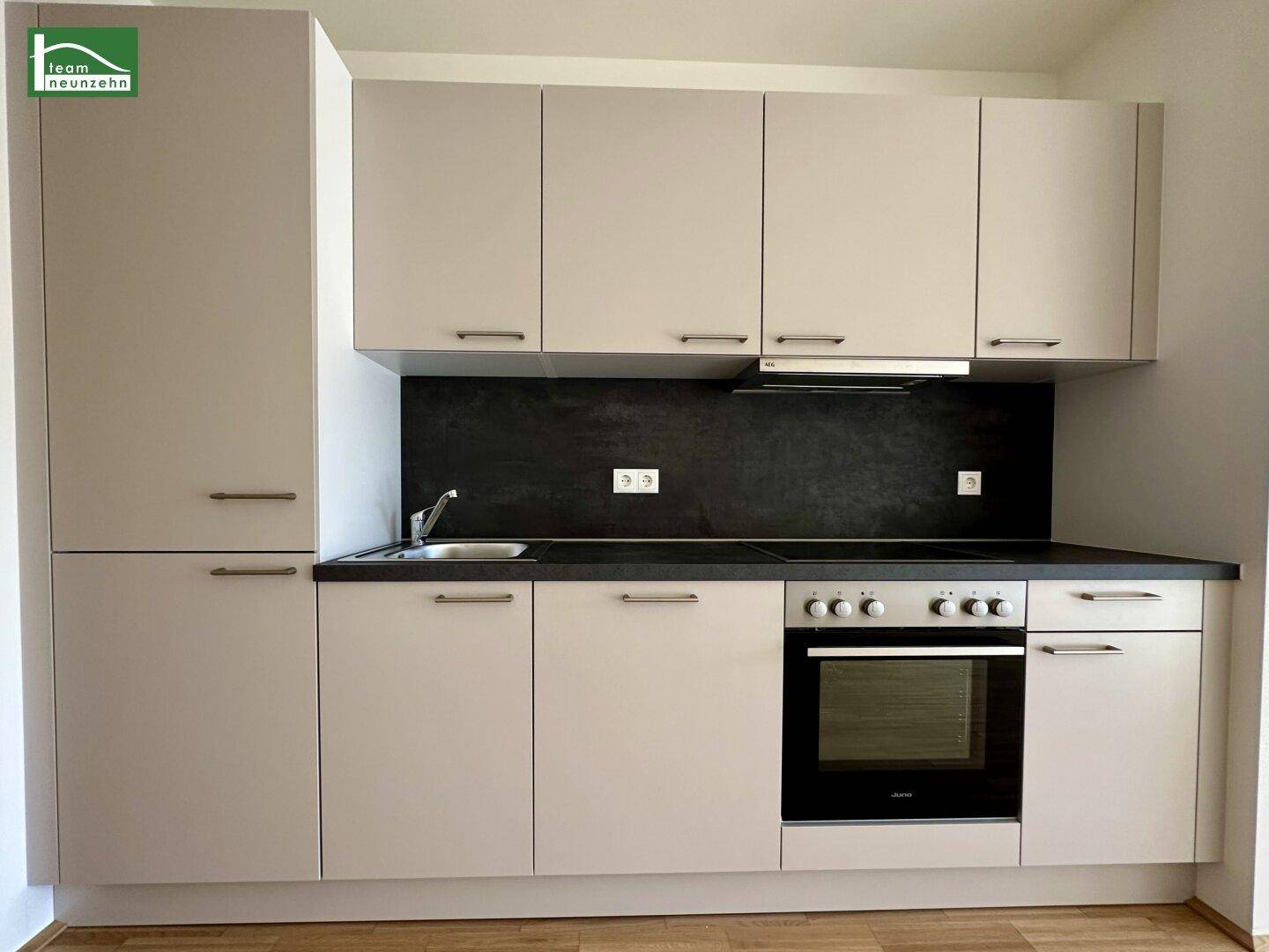Moderne Einbauküche in Beige mit dunkler Arbeitsplatte und integrierten Elektrogeräten.