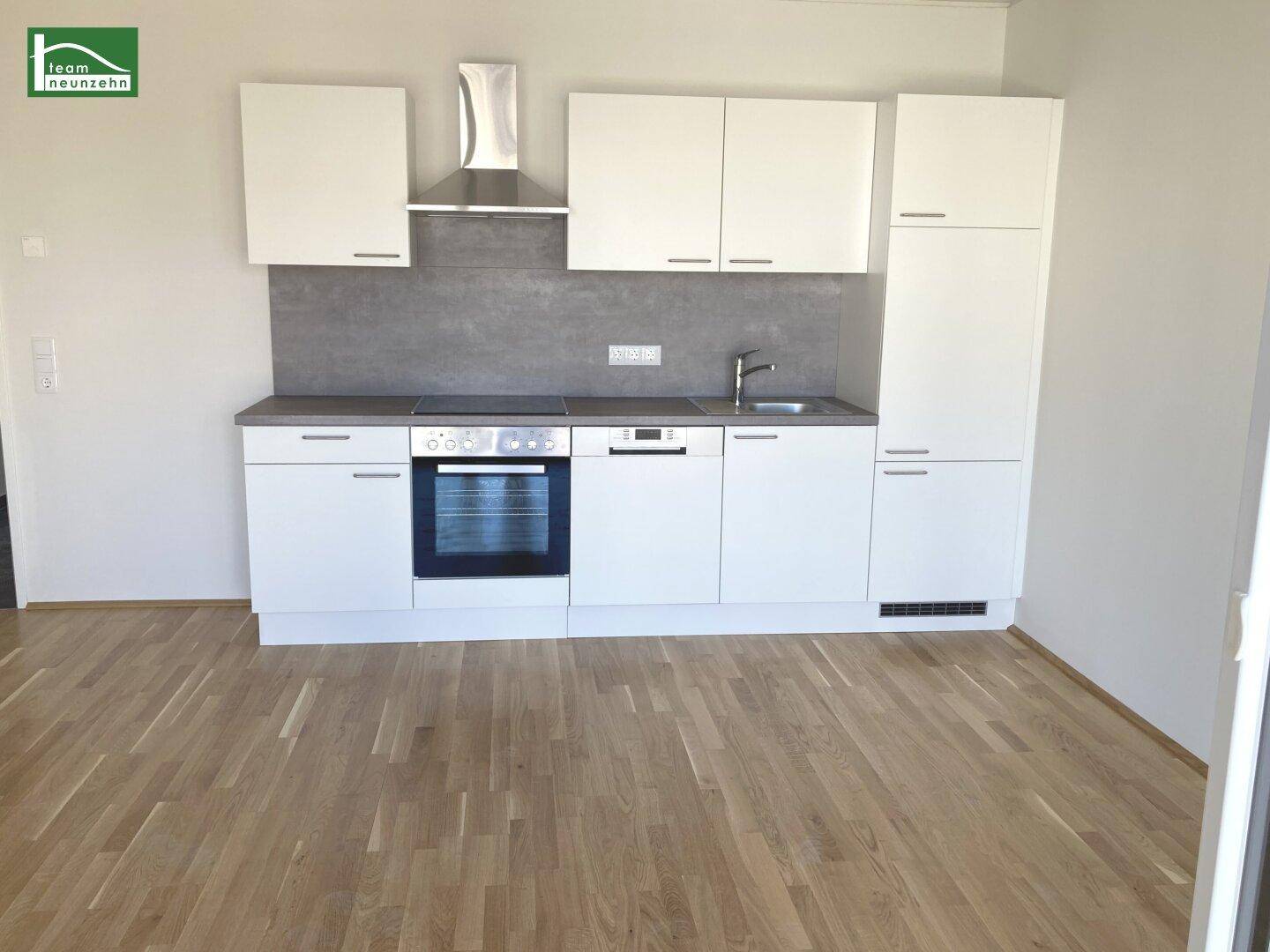 Moderne Einbauküche mit weißen Schränken, Edelstahlgeräten und hellem Parkettboden.