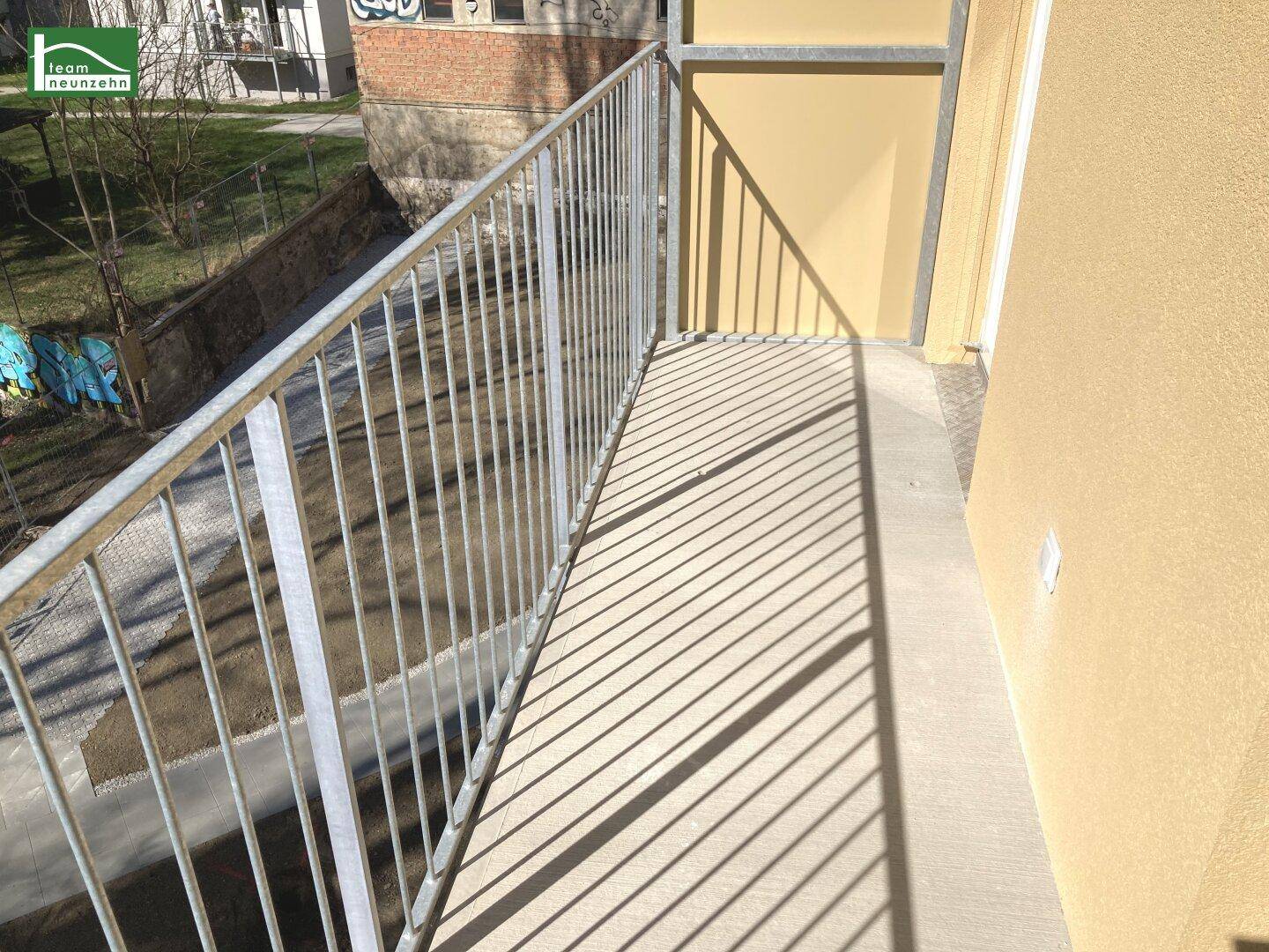 Sonnenbeschienener Balkon mit Metallgeländer und Blick auf die umliegenden Gebäude.