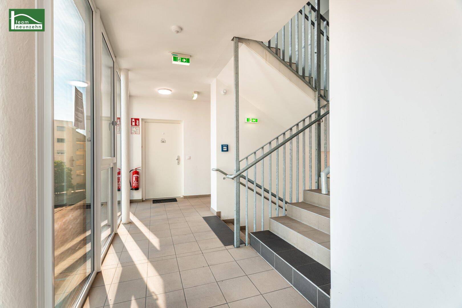 Heller Flur mit Fliesenboden und Treppenhaus mit Metallgeländer im Eingangsbereich.