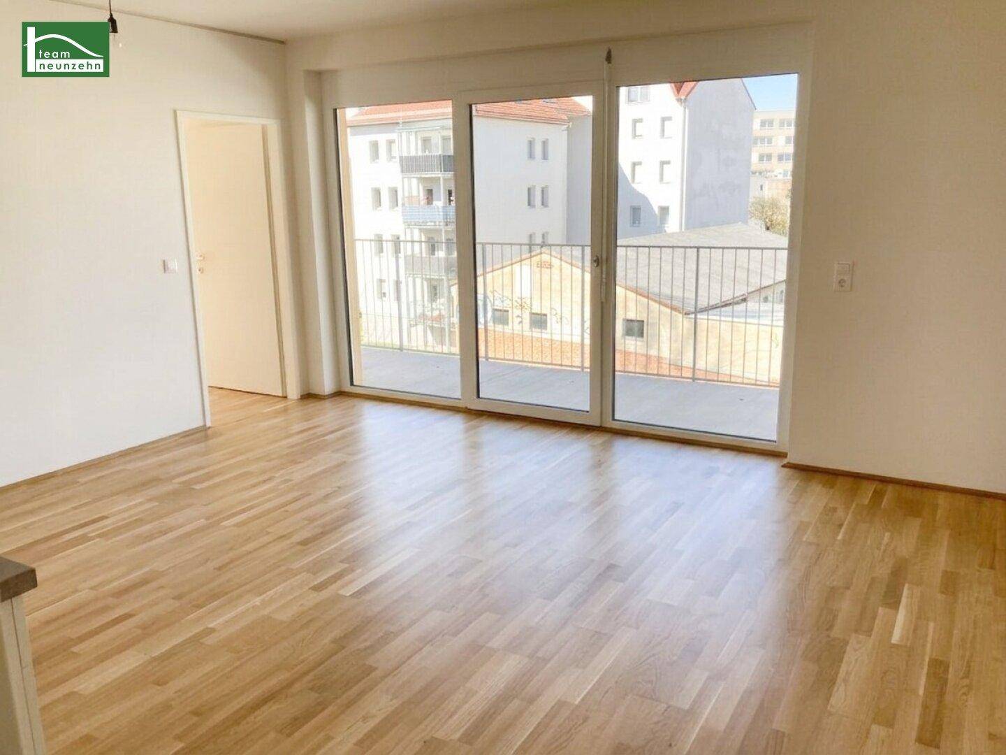 Heller Wohnraum mit Parkettboden und großen Fenstern mit Zugang zu einem Balkon.