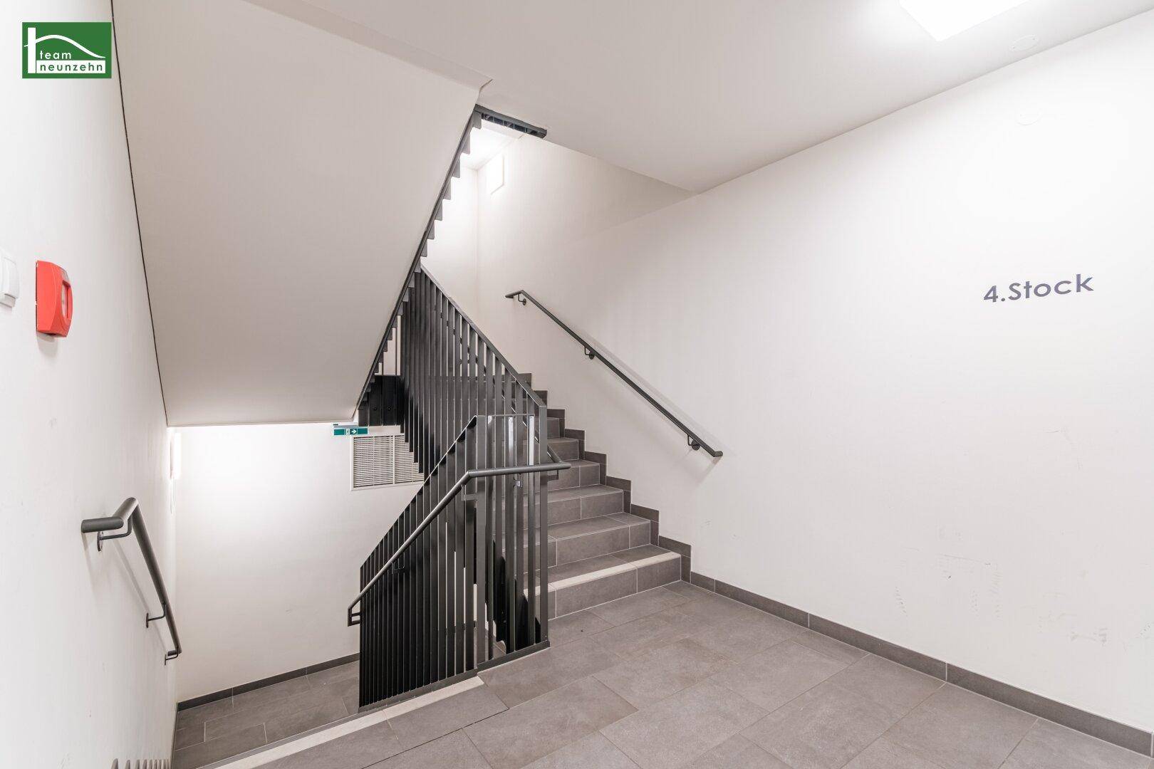 Helles Treppenhaus mit modernem Geländer und Fliesenboden in einem Mehrfamilienhaus.