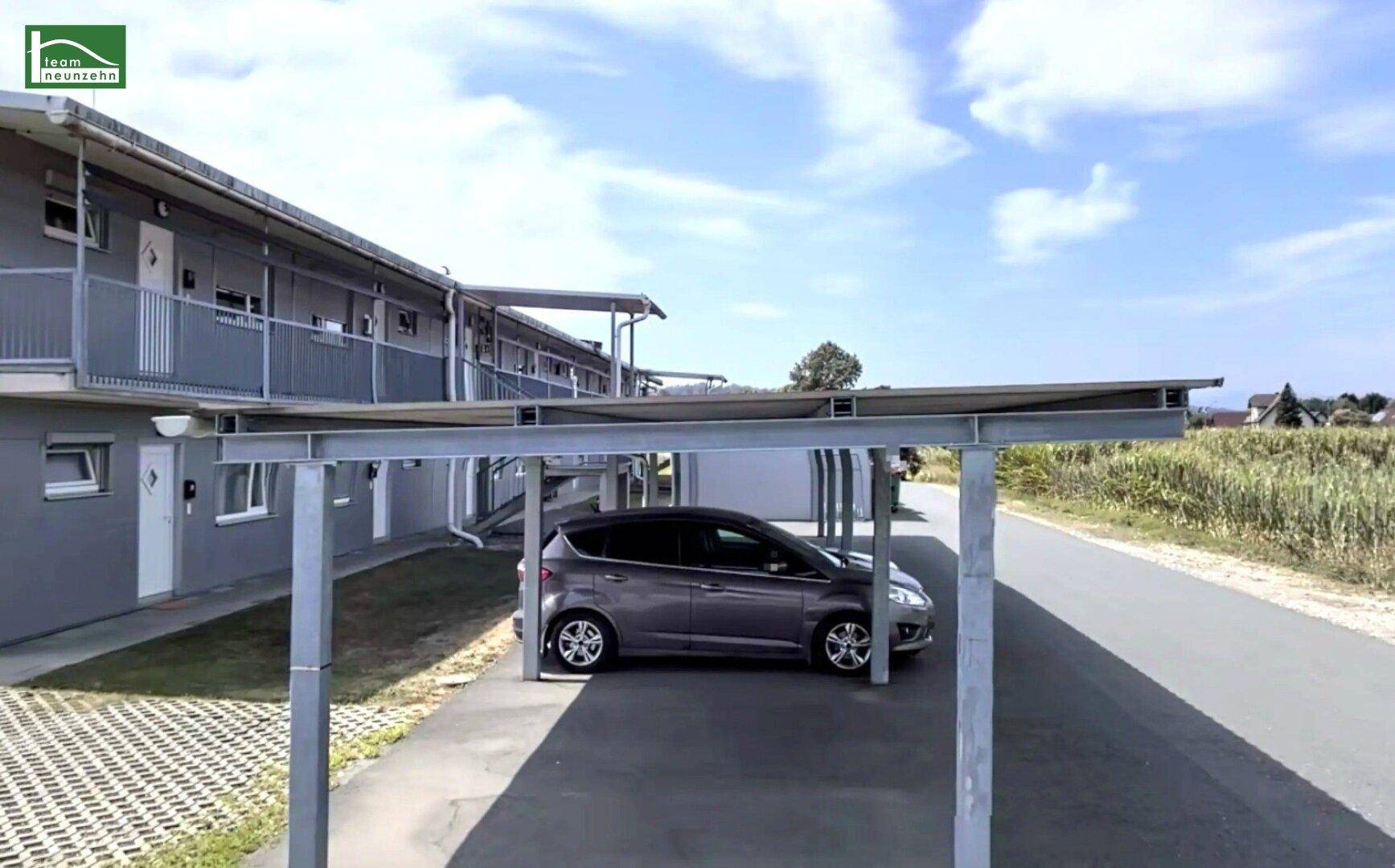 Außenansicht einer Wohnanlage mit überdachten Parkplätzen und einem Auto unter blauem Himmel.